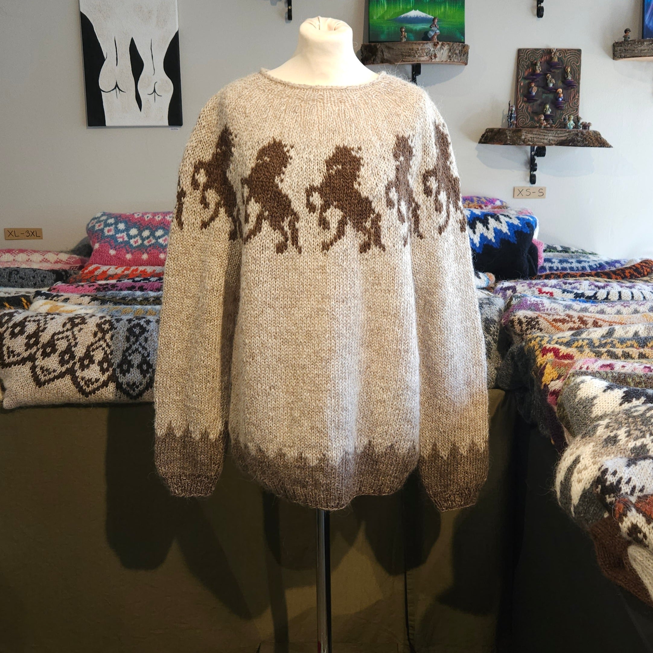Beige sweater with horse patterns on a mannequin against a background of patterned fabric.