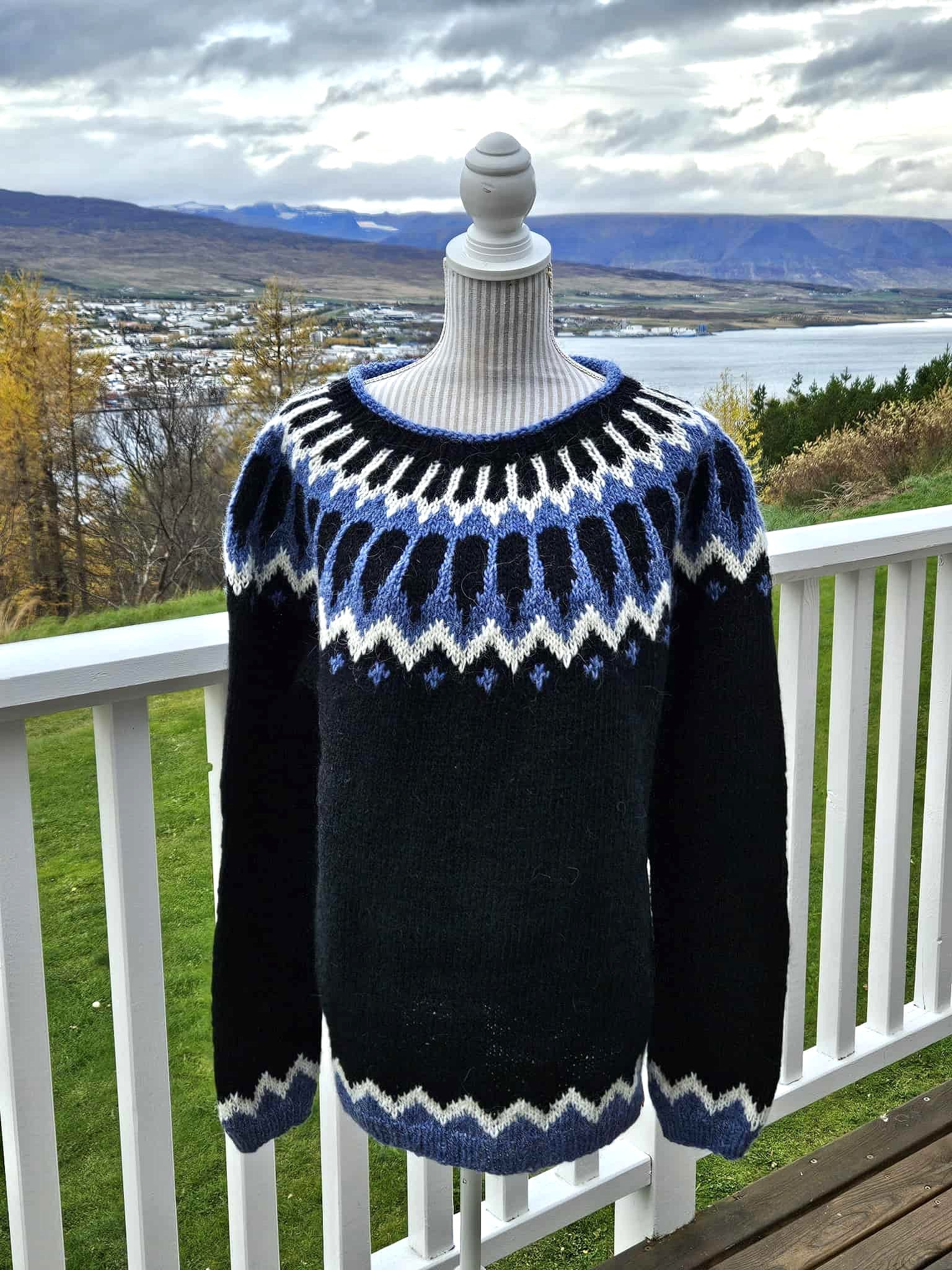 Black sweater with blue and white pattern on a mannequin against a scenic background