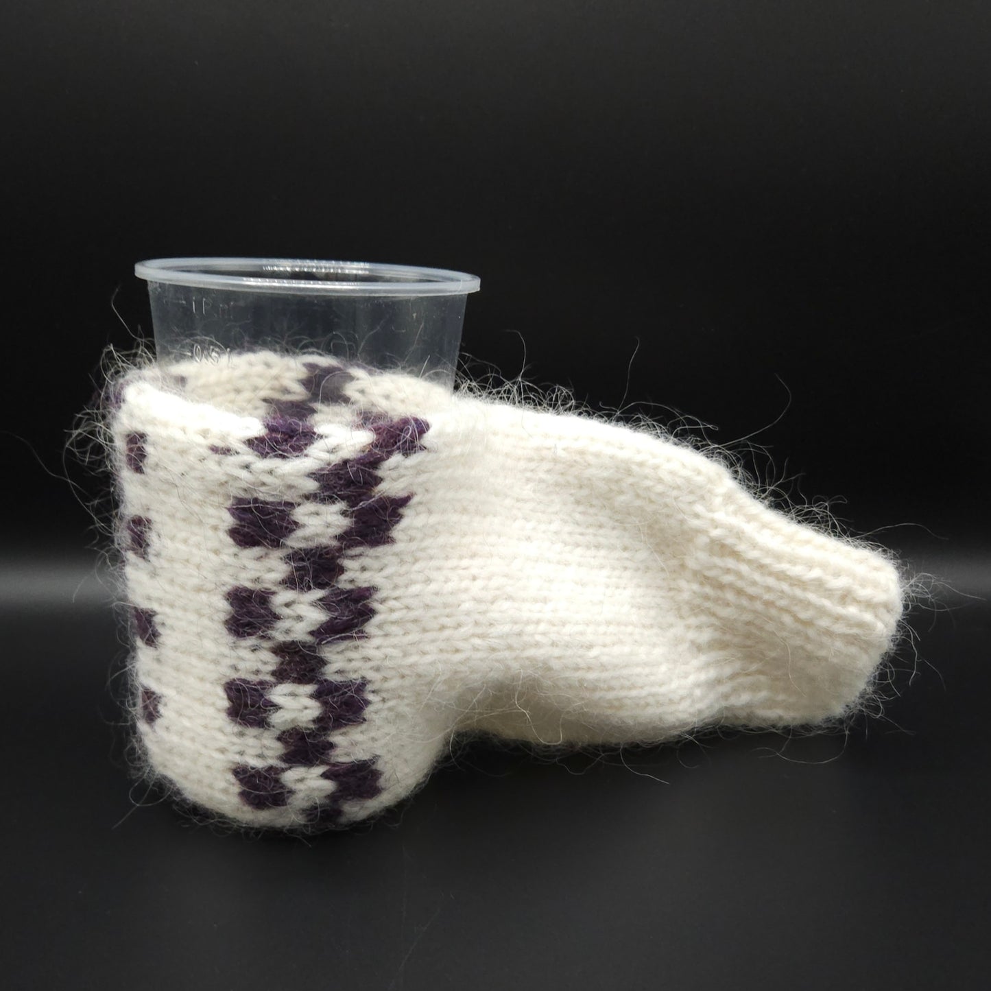 White knitted mitten for holding beer with purple pattern with a black background