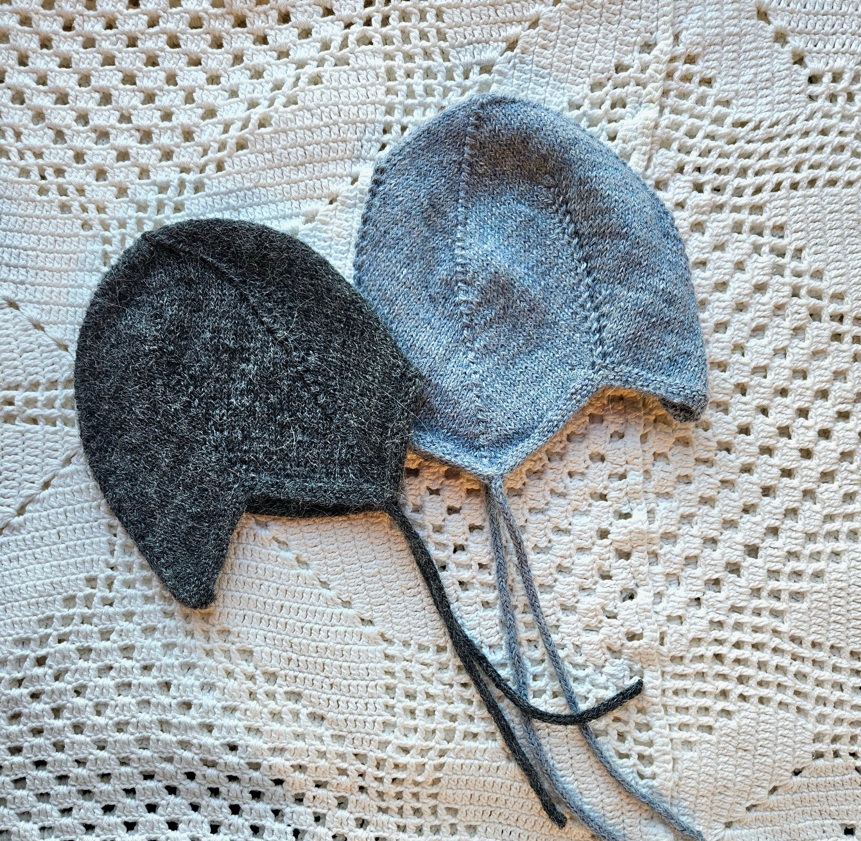 Two knitted baby hats, one black and one gray, on a textured white surface.