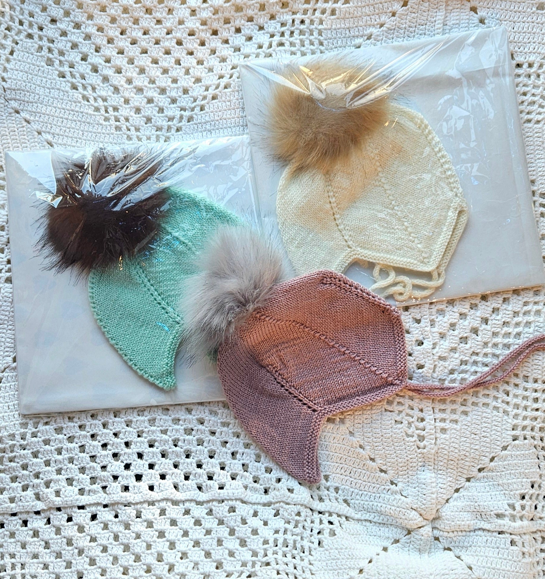 Knitted hats with pom-poms on a textured white surface