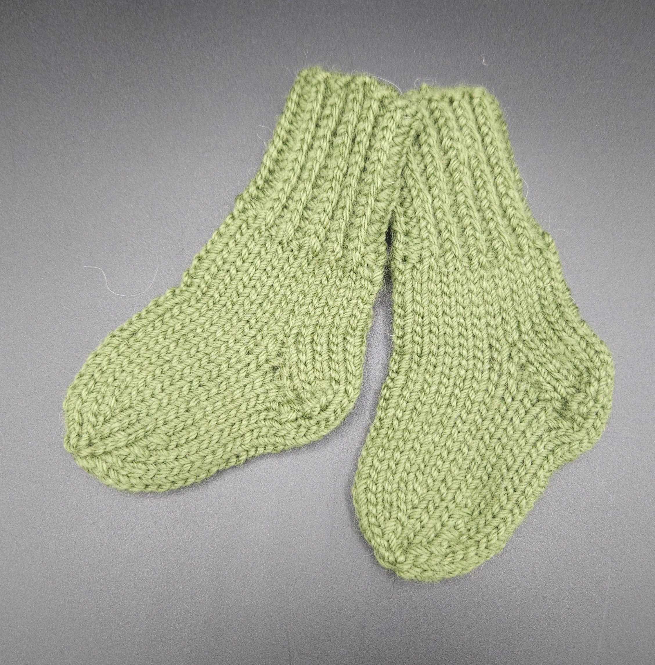 Pair of green knitted socks on a gray background