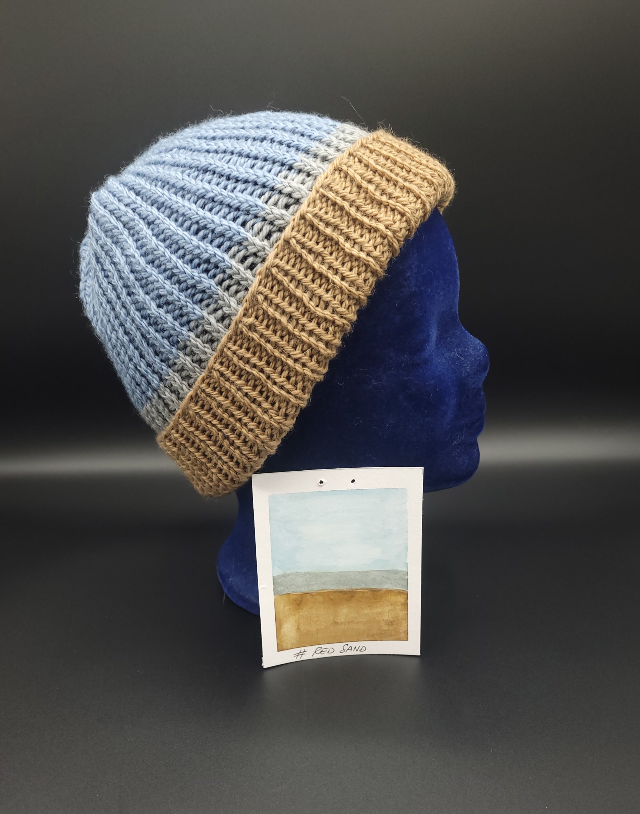Knitted beanie with blue and brown pattern on a mannequin head against a dark background