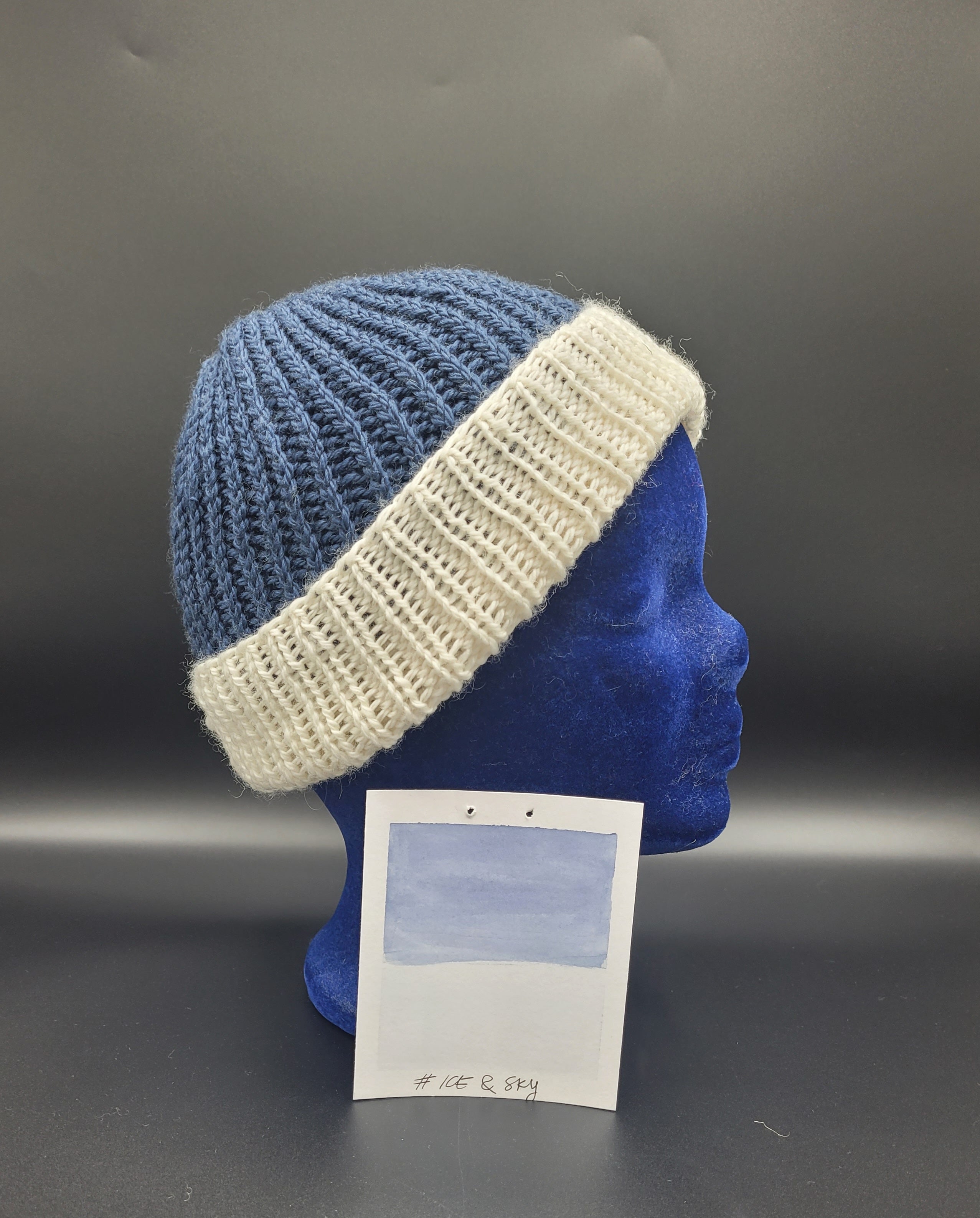 Blue and white knitted beanie on a mannequin head with a gray background