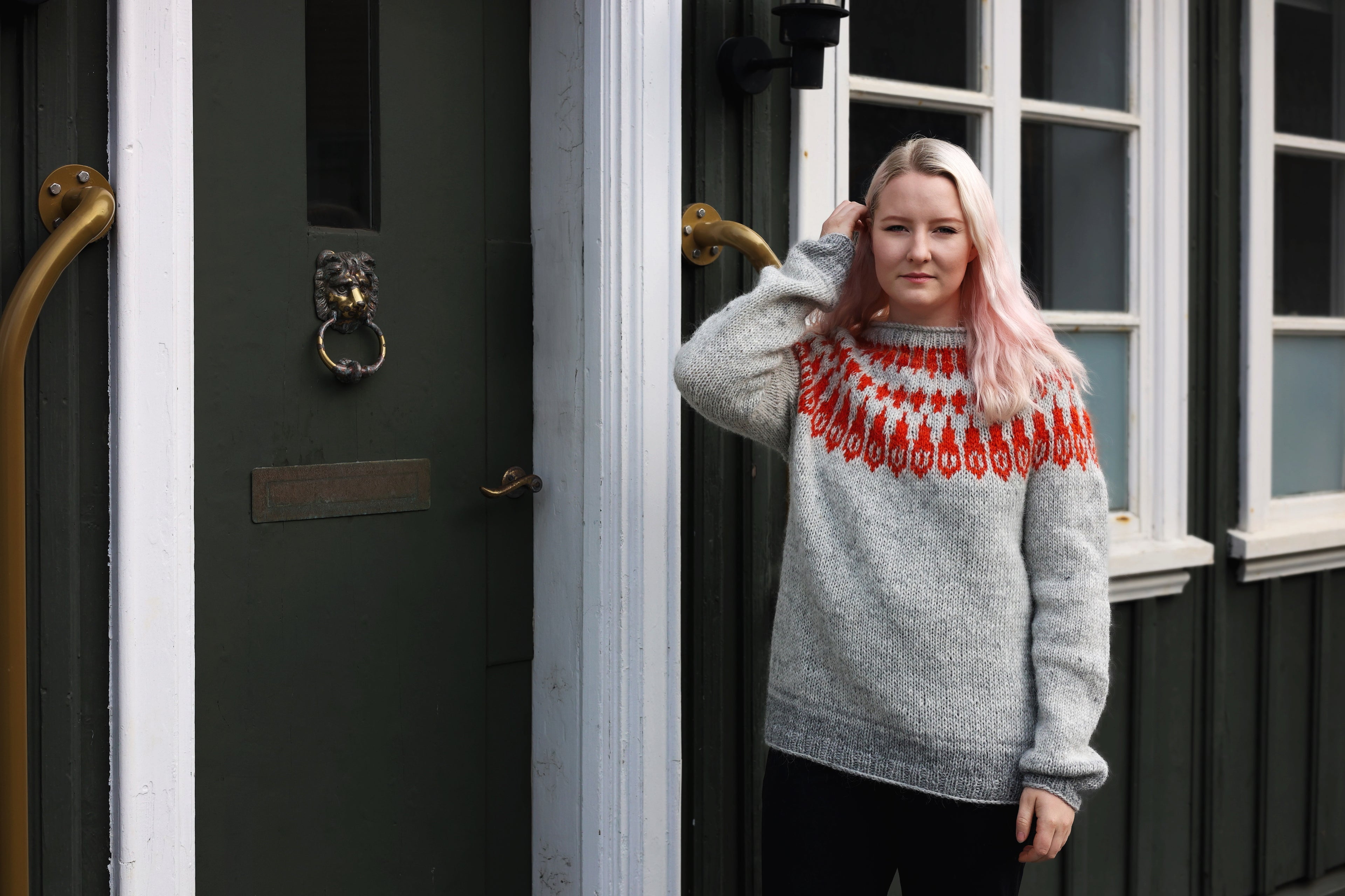 A person standing outside wearing a gray Icelandic wool sweater with a traditional red and white pattern around the neckline.