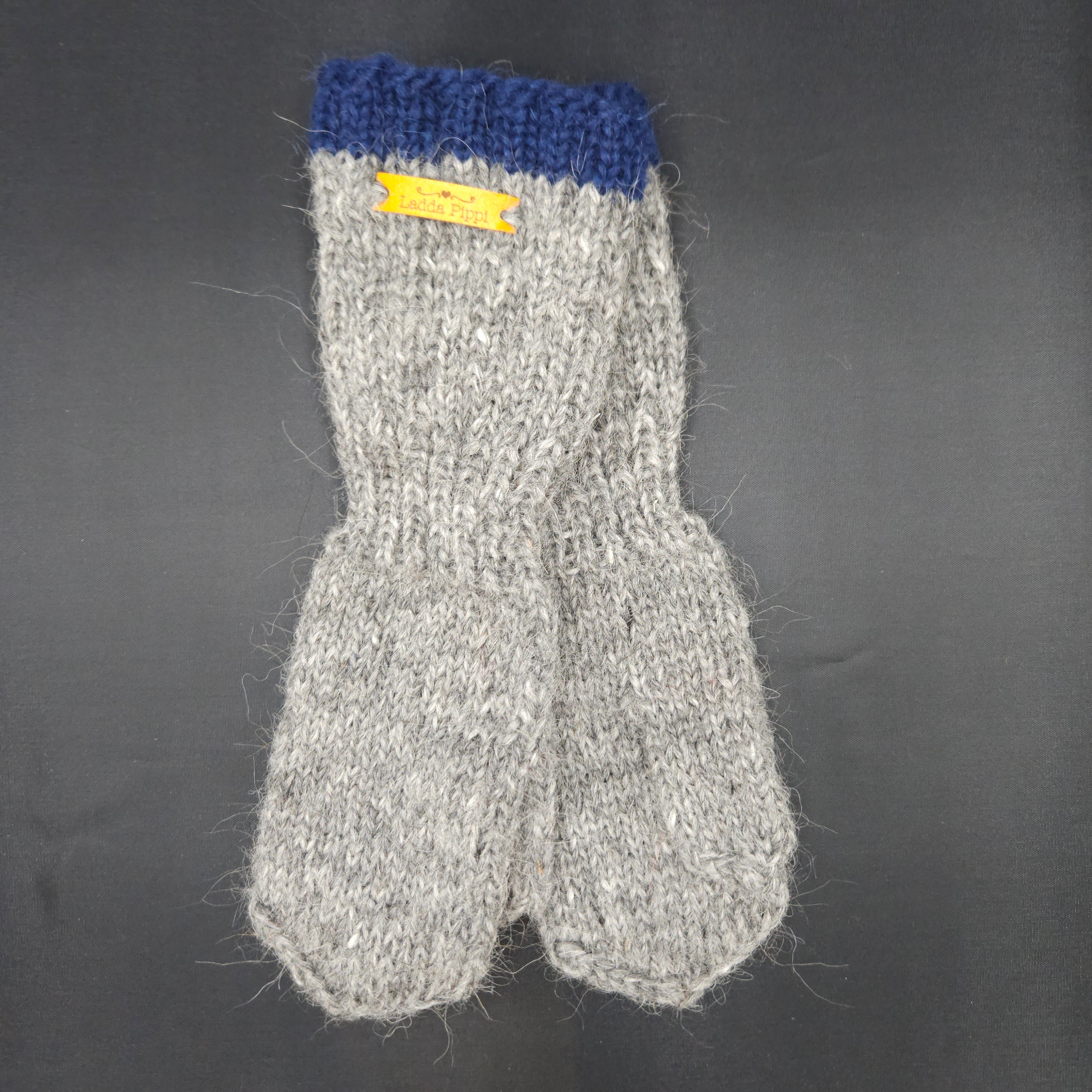Gray knit mittens with blue cuff and yellow label on a dark background
