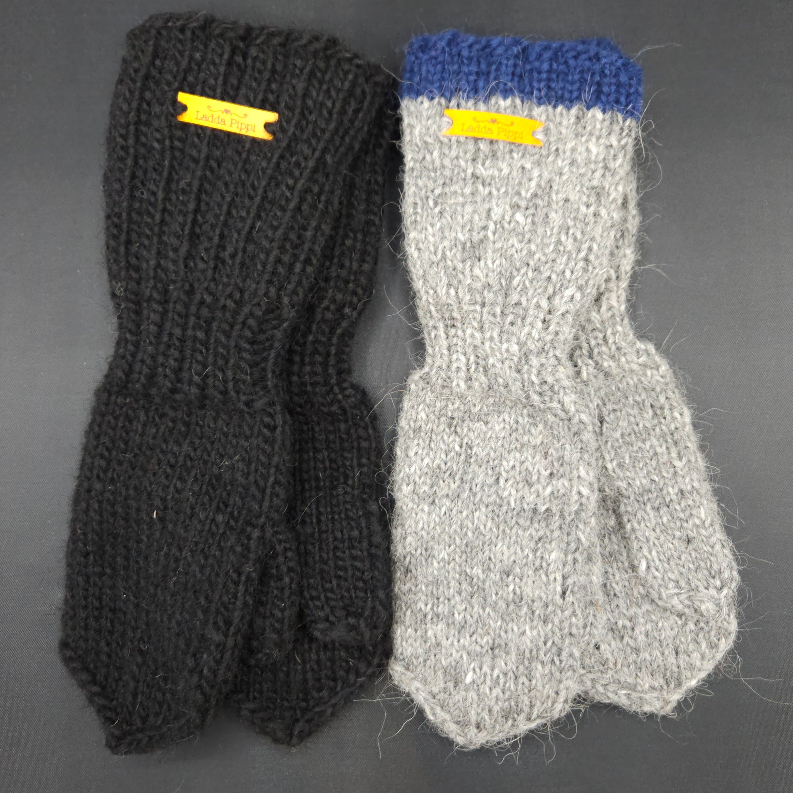 Knitted mittens, one black and one gray with blue cuff, on a dark background.