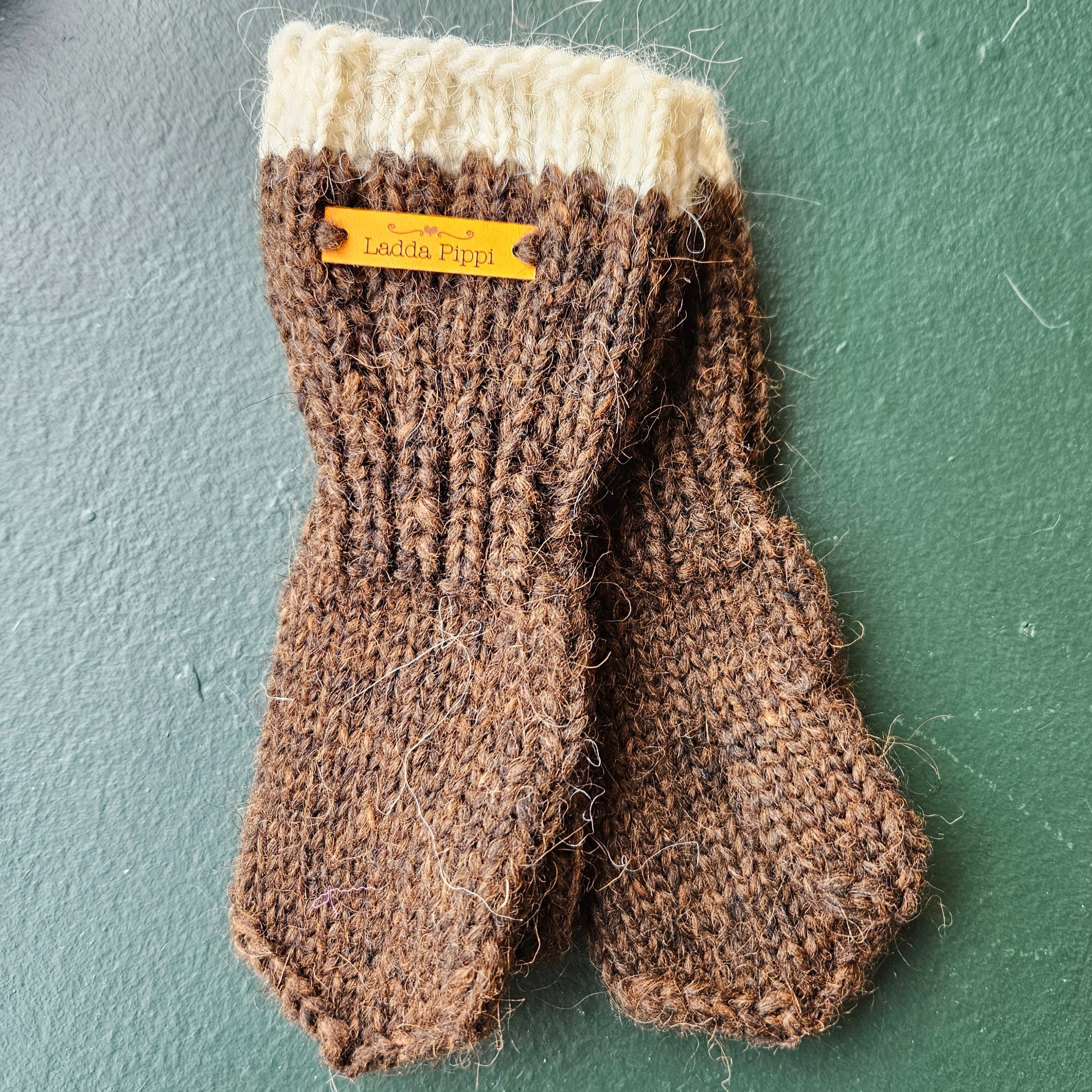 Pair of brown knitted mittens with a white cuff on a green background