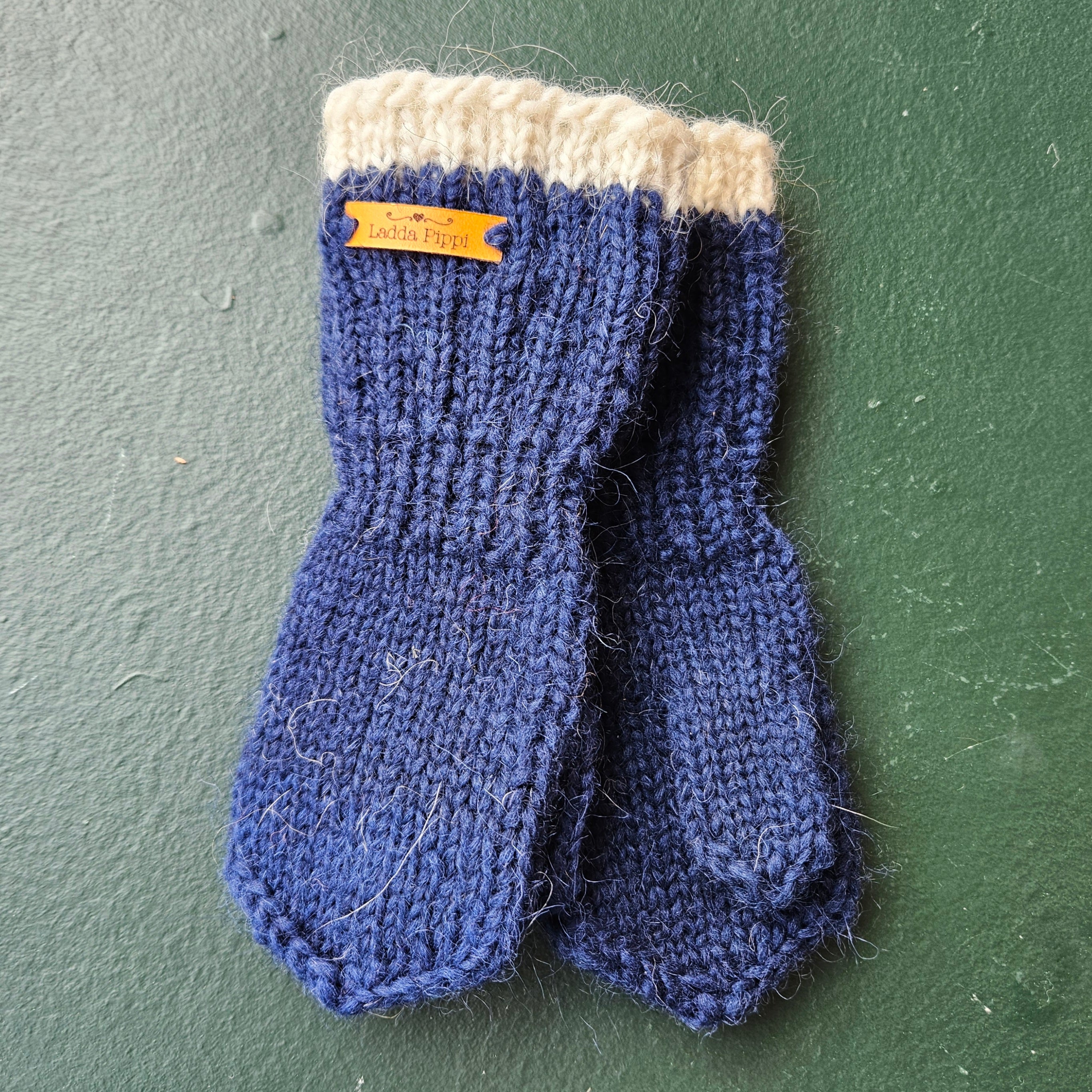 Pair of blue knitted mittens with a white cuff on a green background