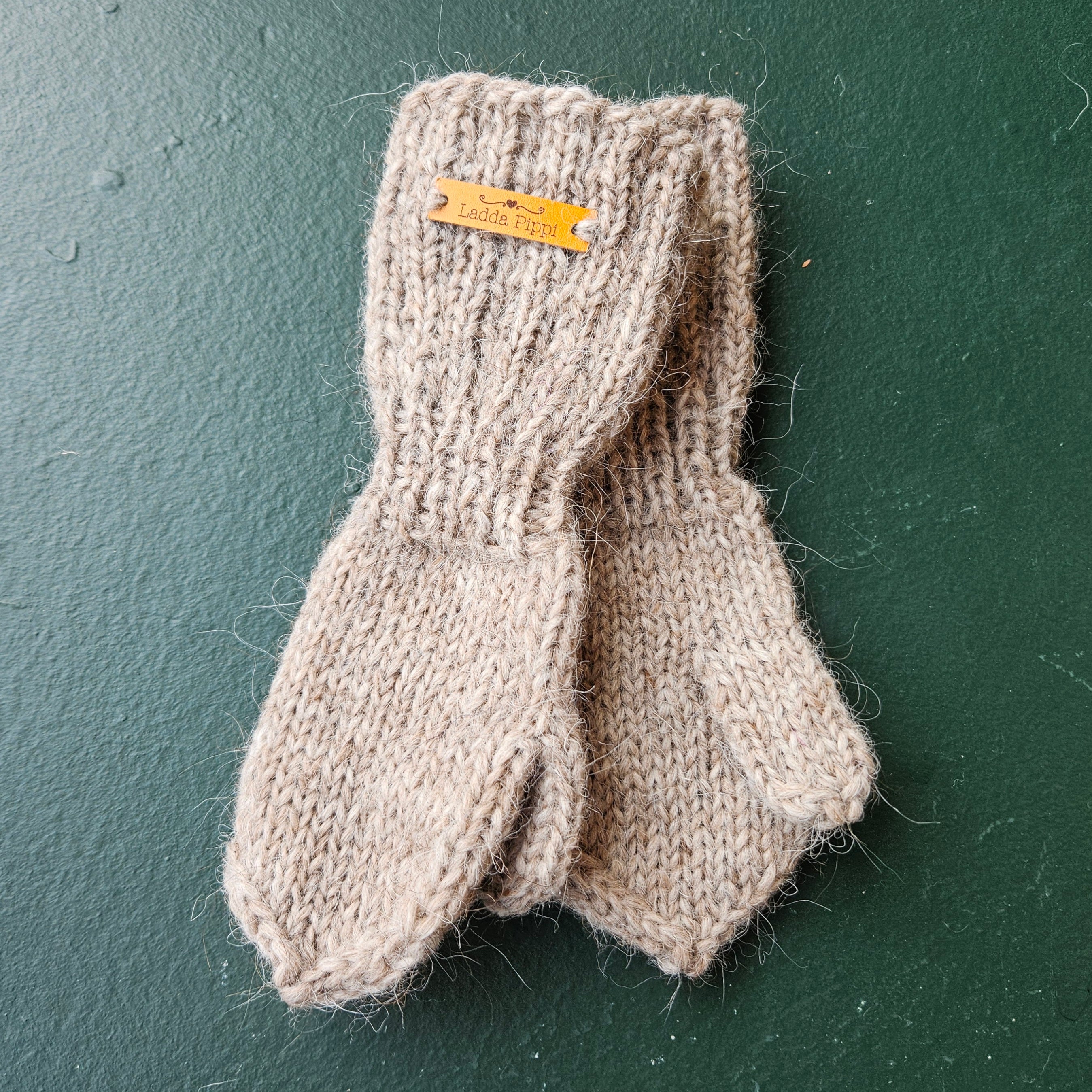 Pair of beige knitted mittens with a brand tag on a dark green background