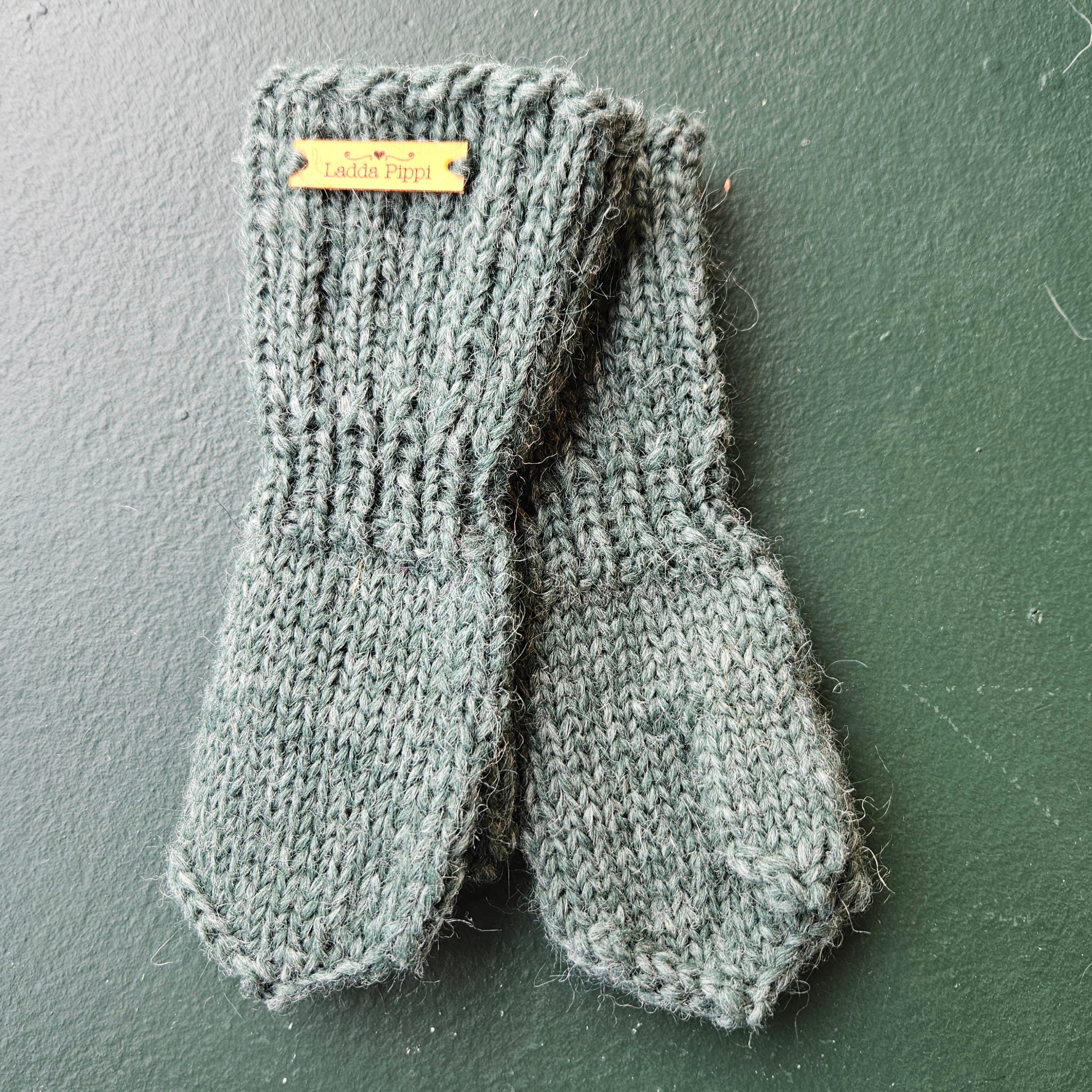 Pair of green knitted mittens with a brand label on a dark green background