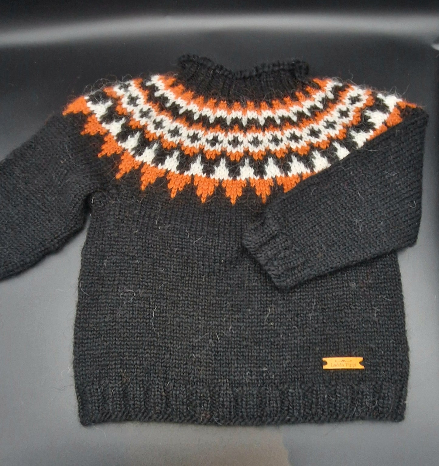 Black hand-knit Icelandic wool sweater featuring a traditional Nordic pattern in white and orange colors on a black surface