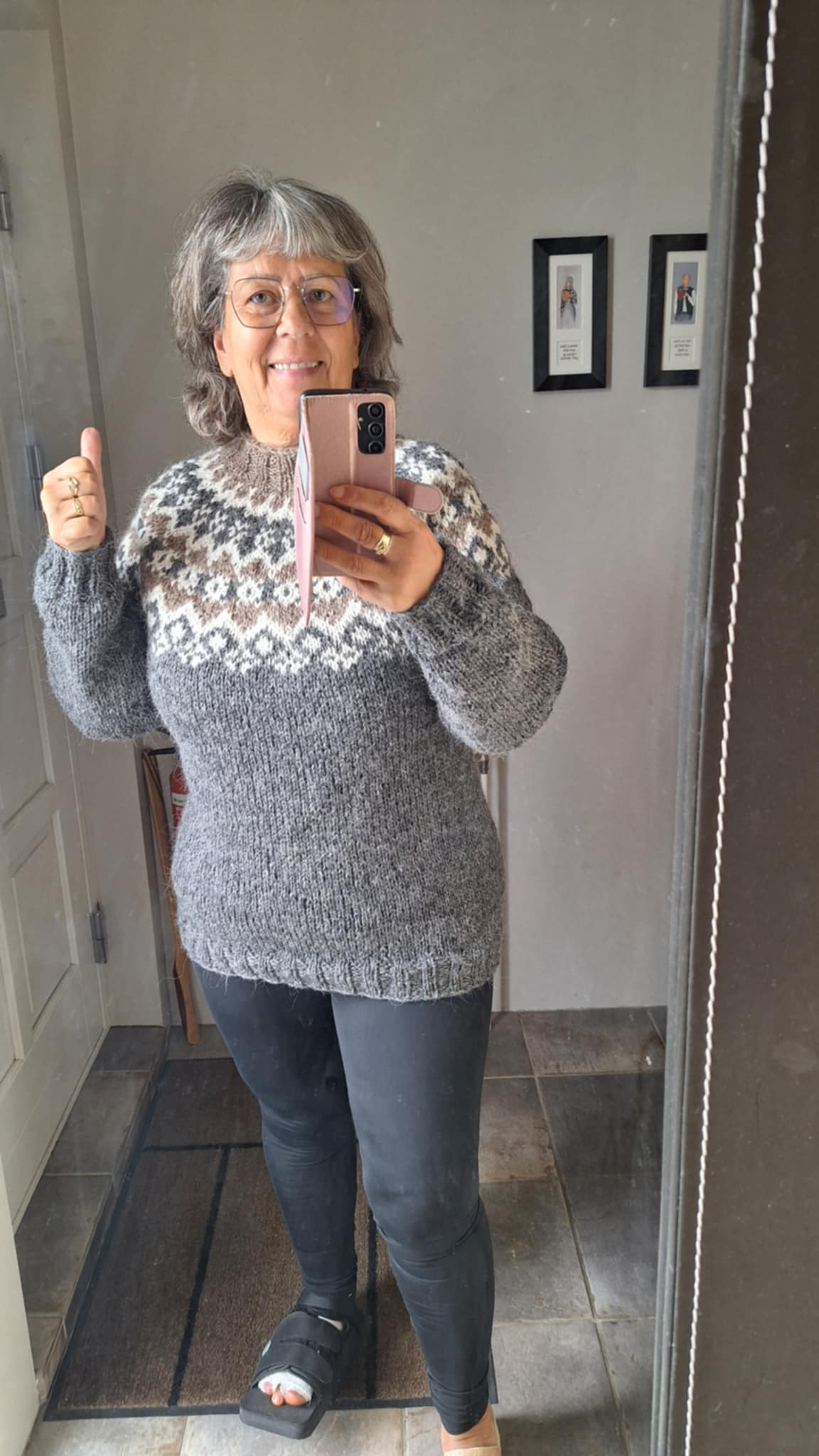 Person wearing a gray hand-knit Icelandic wool sweater with a traditional Nordic patterned sweater taking a mirror selfie indoors.