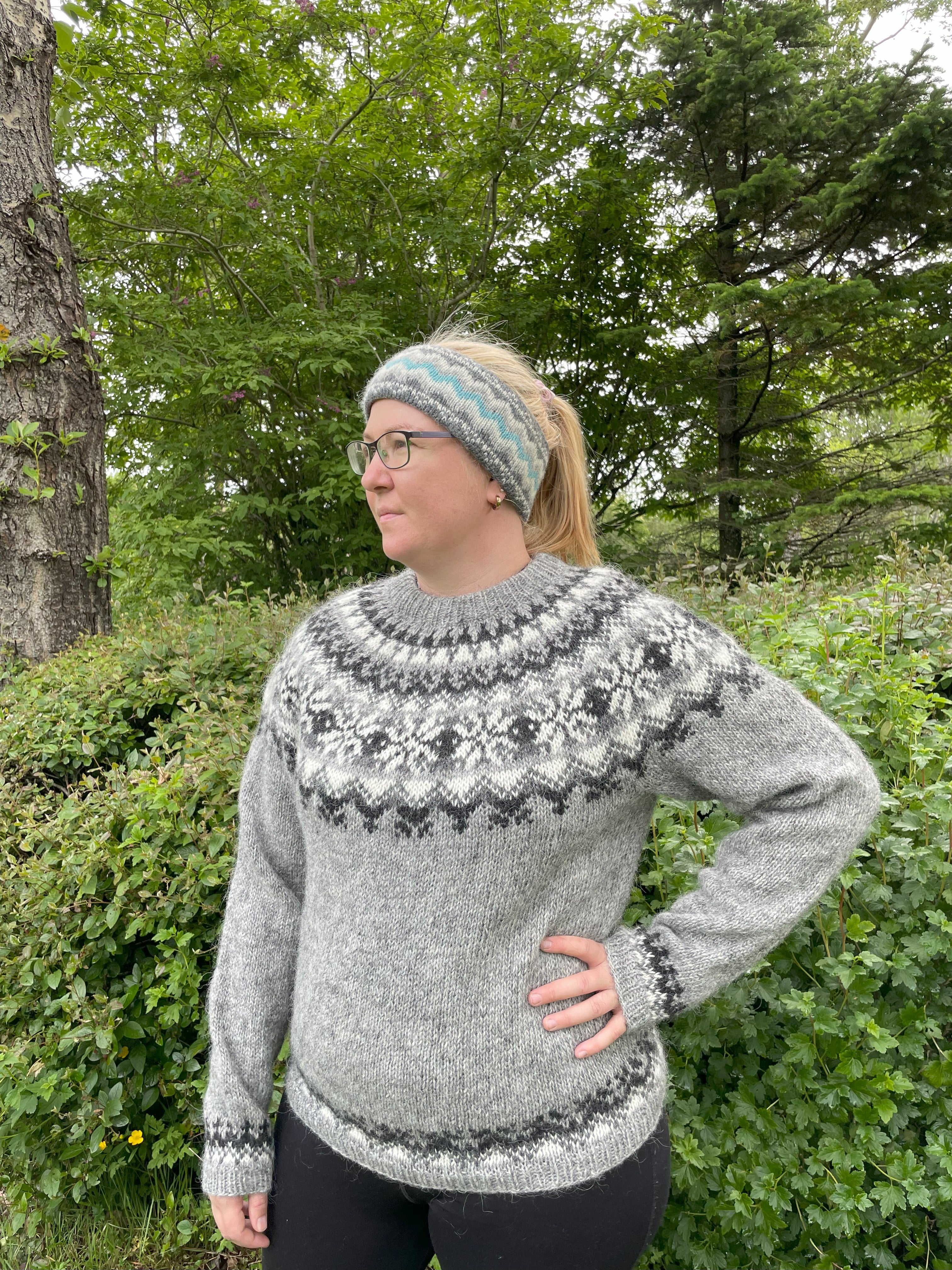 Person wearing a patterned sweater and headband outdoors with trees in the background
