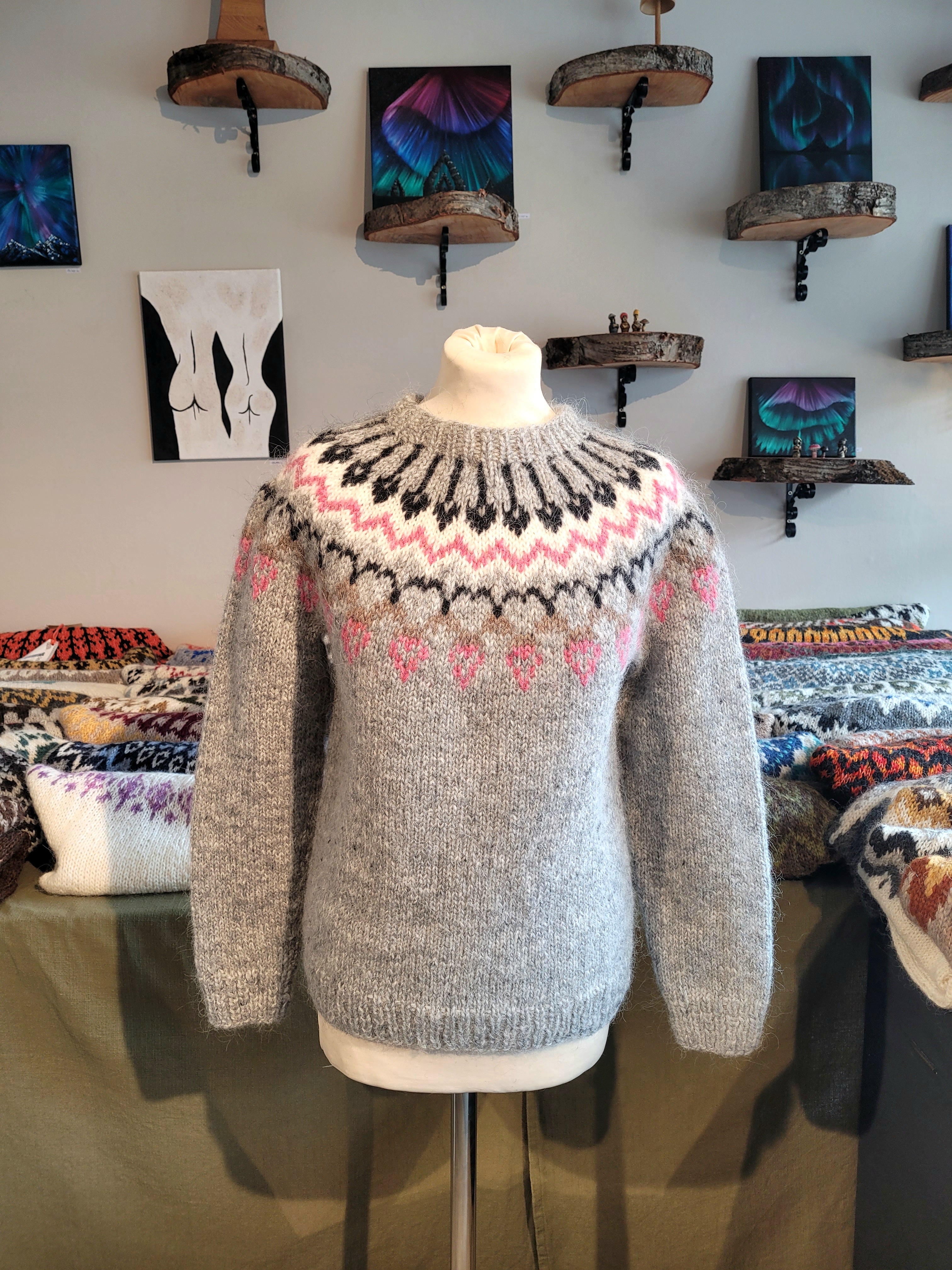 Gray hand-knit Icelandic wool sweater featuring a traditional Nordic pattern in  white, black, and pink colors on a mannequin in a store setting