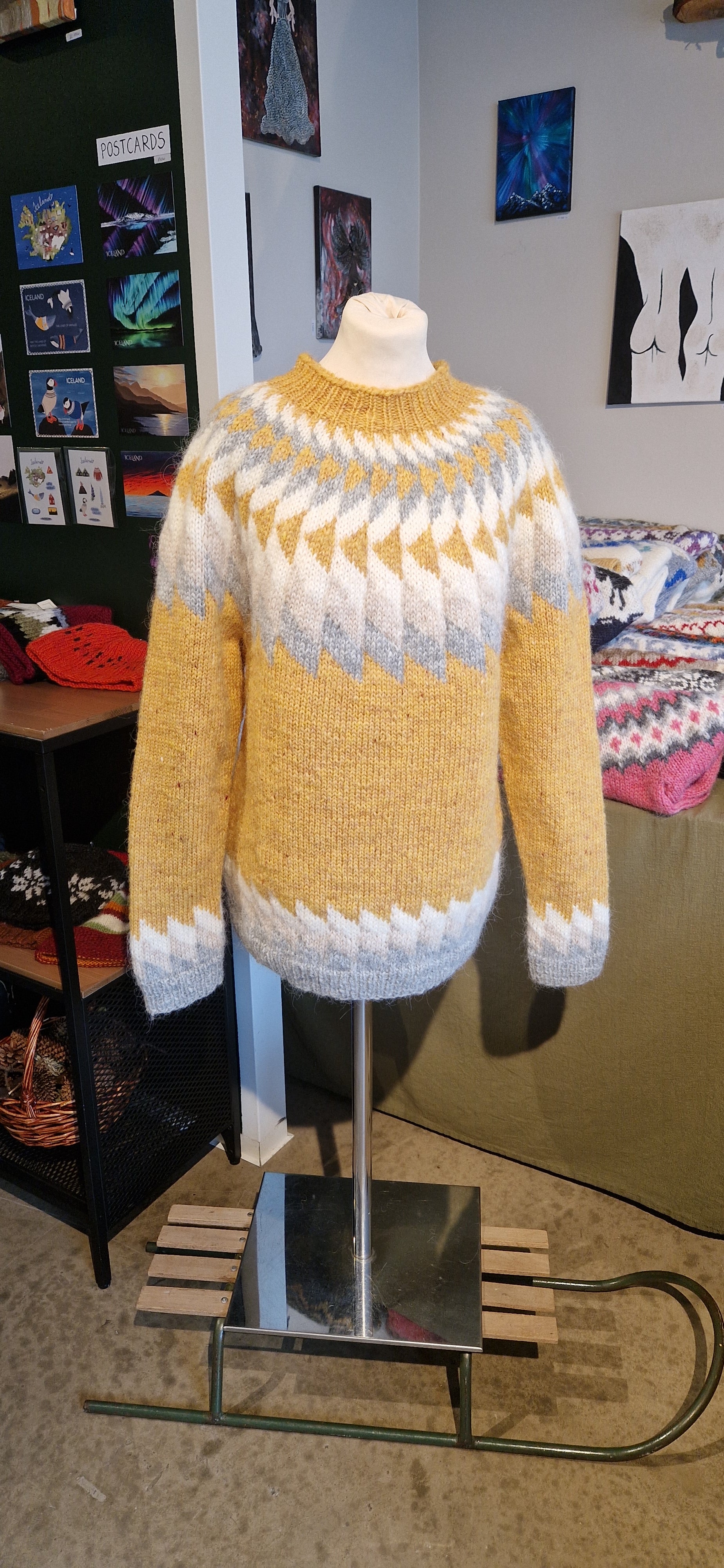 A mannequin in a yellow hand-knit Icelandic wool sweater featuring a traditional Nordic pattern in white and gray in a store setting.