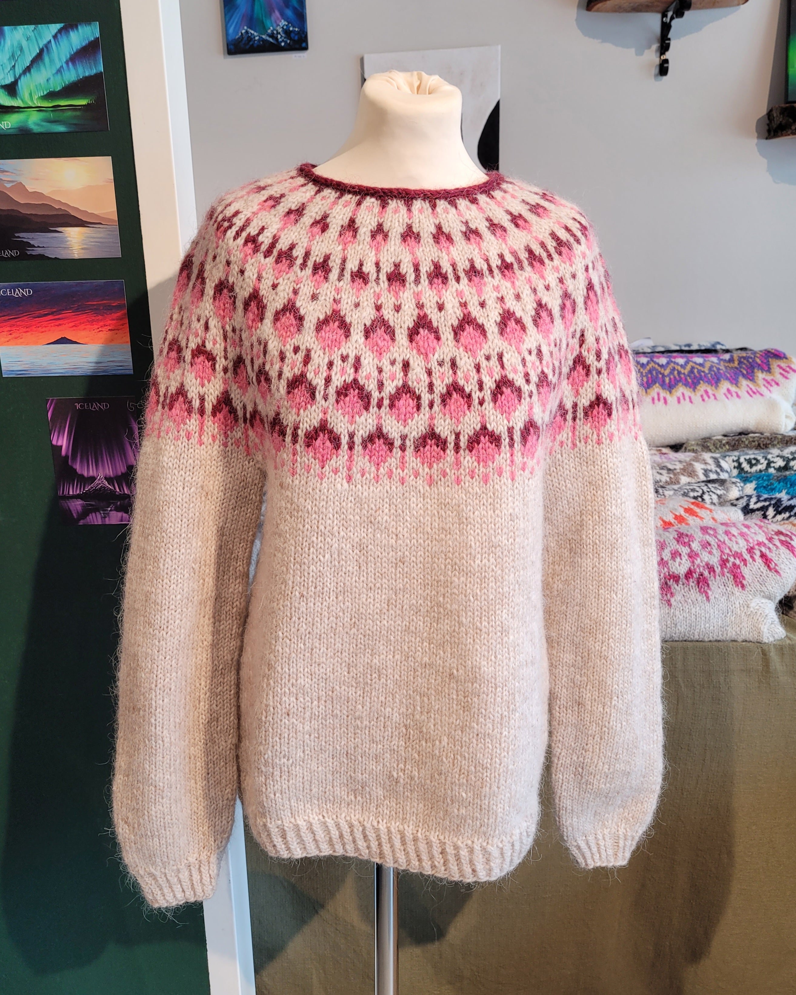 A mannequin in a beige hand-knit Icelandic wool sweater featuring a traditional Nordic pattern in pink in a store setting.