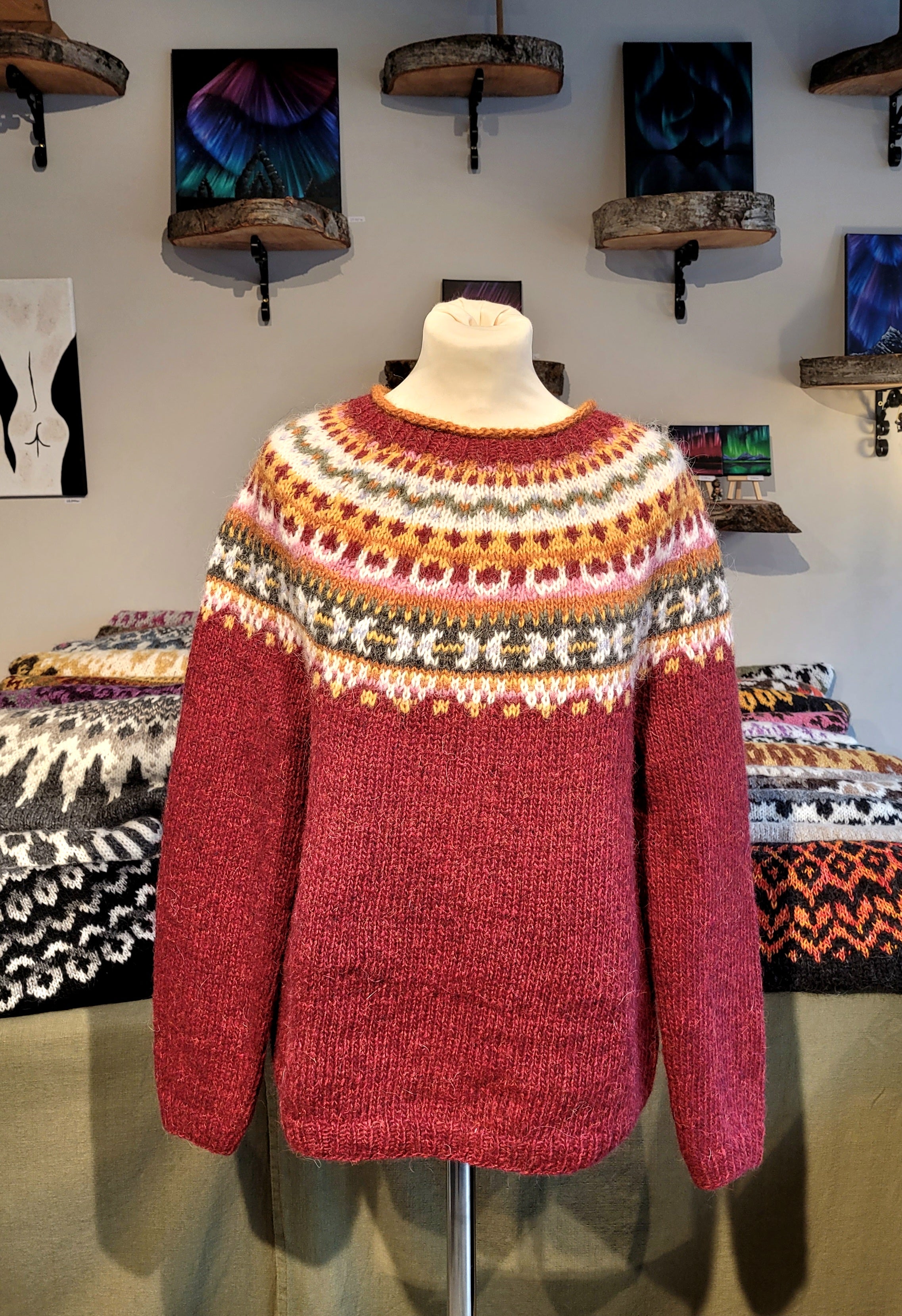A mannequin in a red hand-knit Icelandic wool sweater featuring a traditional Nordic pattern in multiple colors in a store setting.