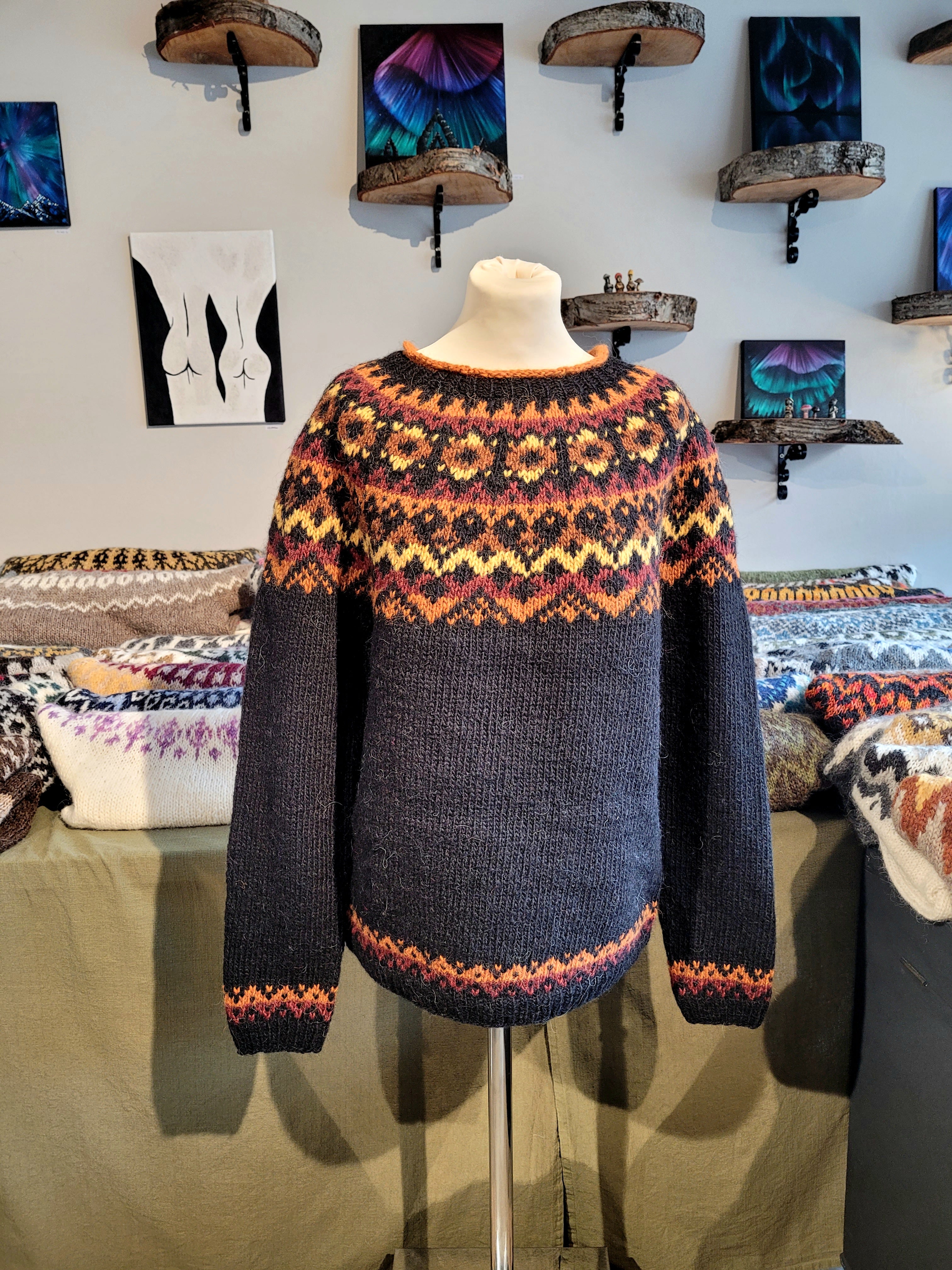 A mannequin in a black hand-knit Icelandic wool sweater featuring a traditional Nordic pattern in orange and yellow in a store setting.