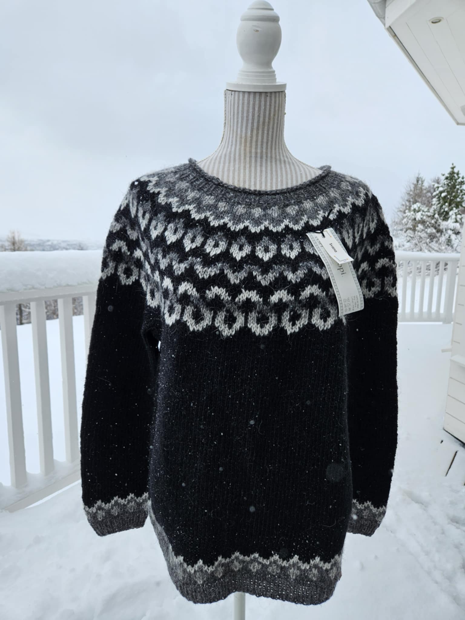 A black and gray hand knit Icelandic wool sweater displayed on a mannequin outdoors, with snow visible in the background.
