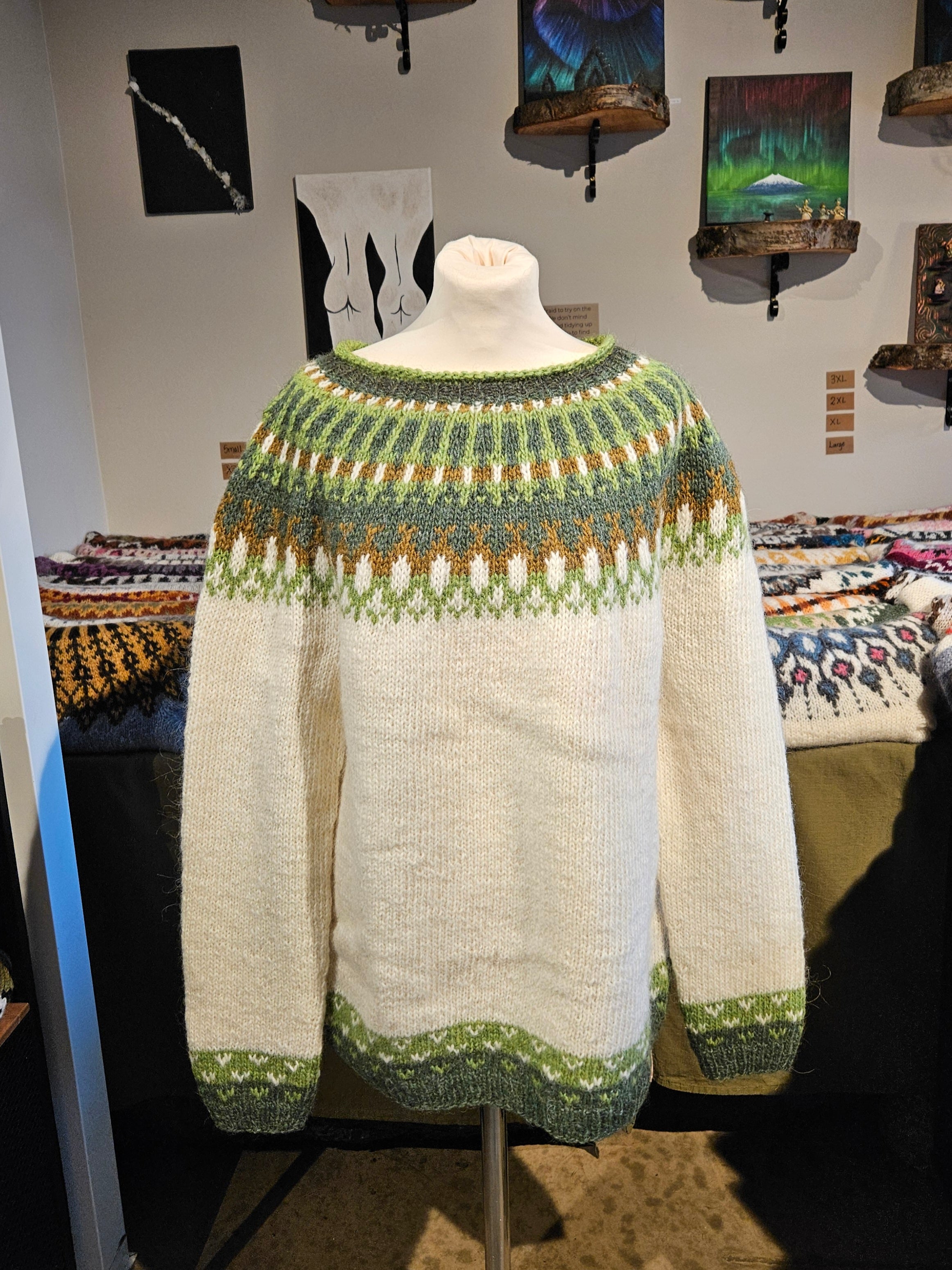 Knitted sweater on a mannequin in a store setting with various knitted items and artwork in the background.