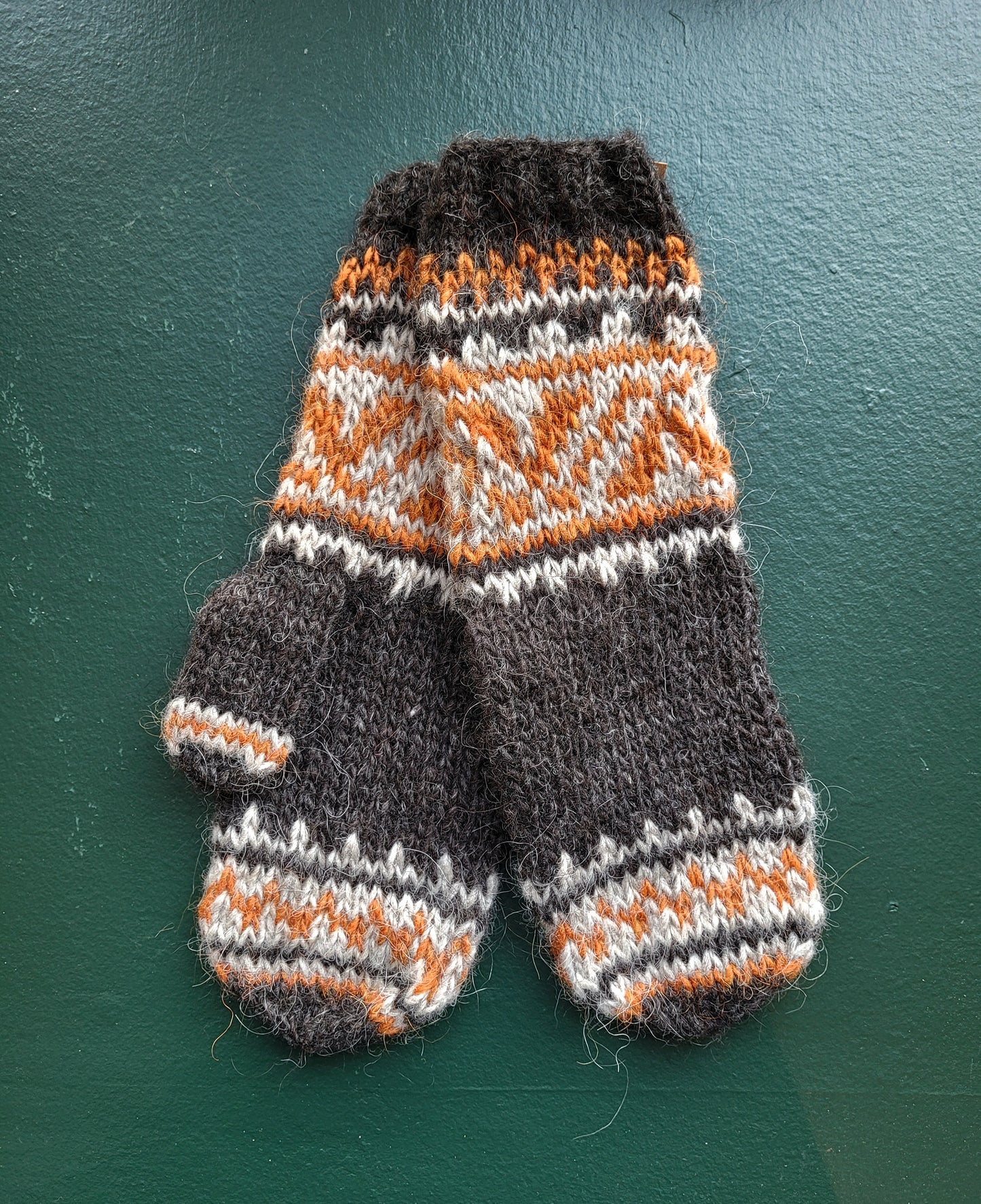 Pair of knitted mittens with a geometric pattern on a green background