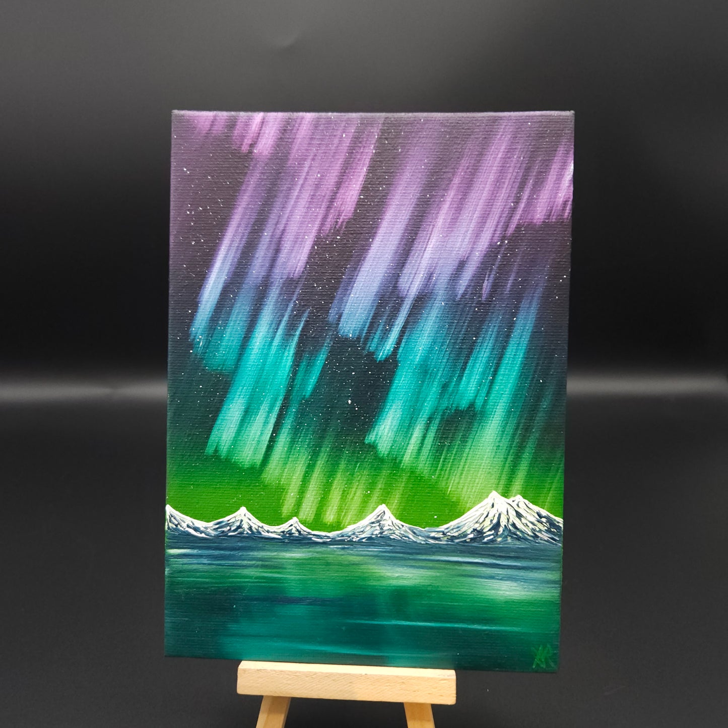Northern lights landscape painting featuring pink, blue and green northern lights over snow-capped mountains reflected in water.