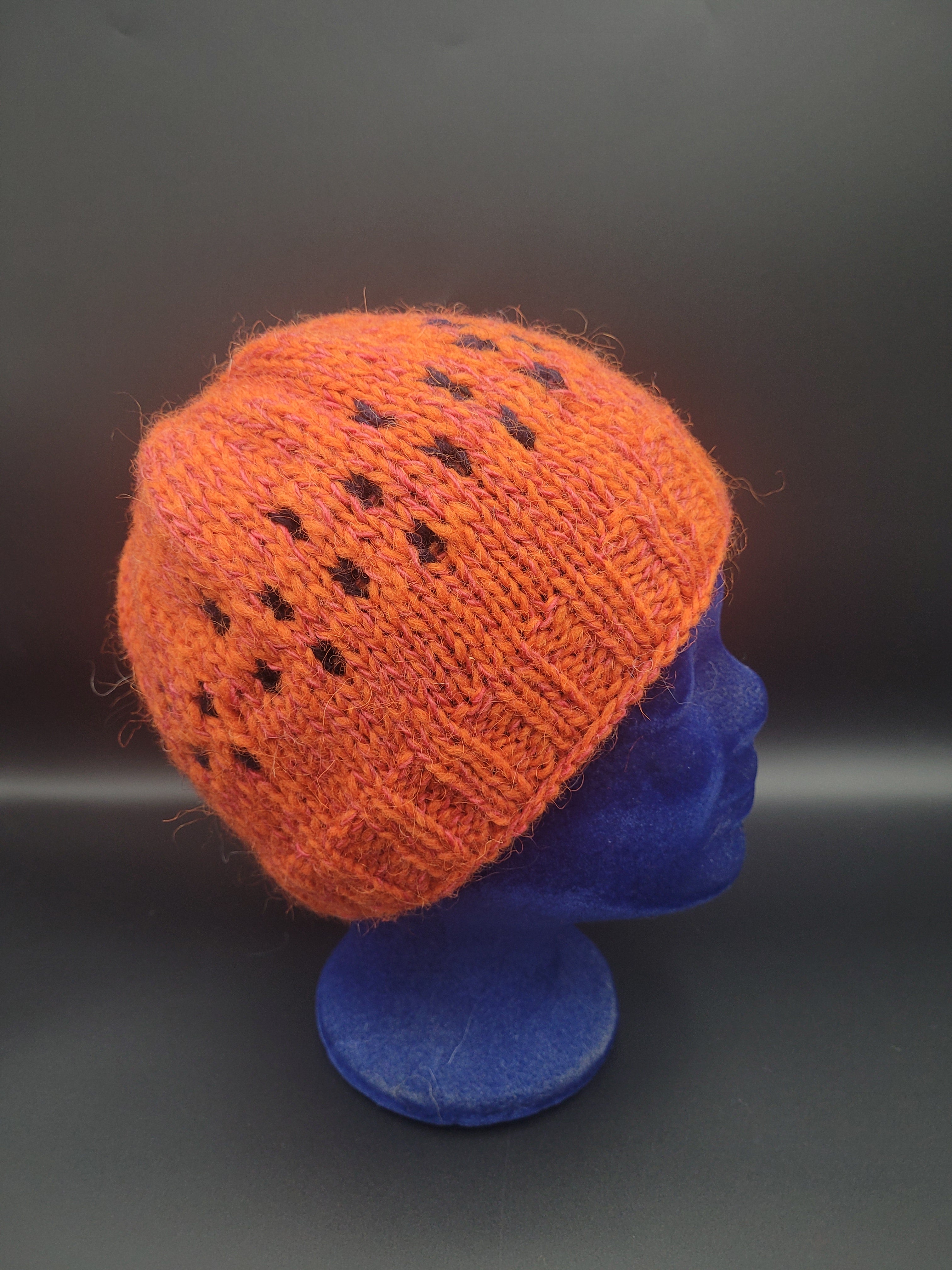 Knitted orange hat with black dot pattern on a blue mannequin head.