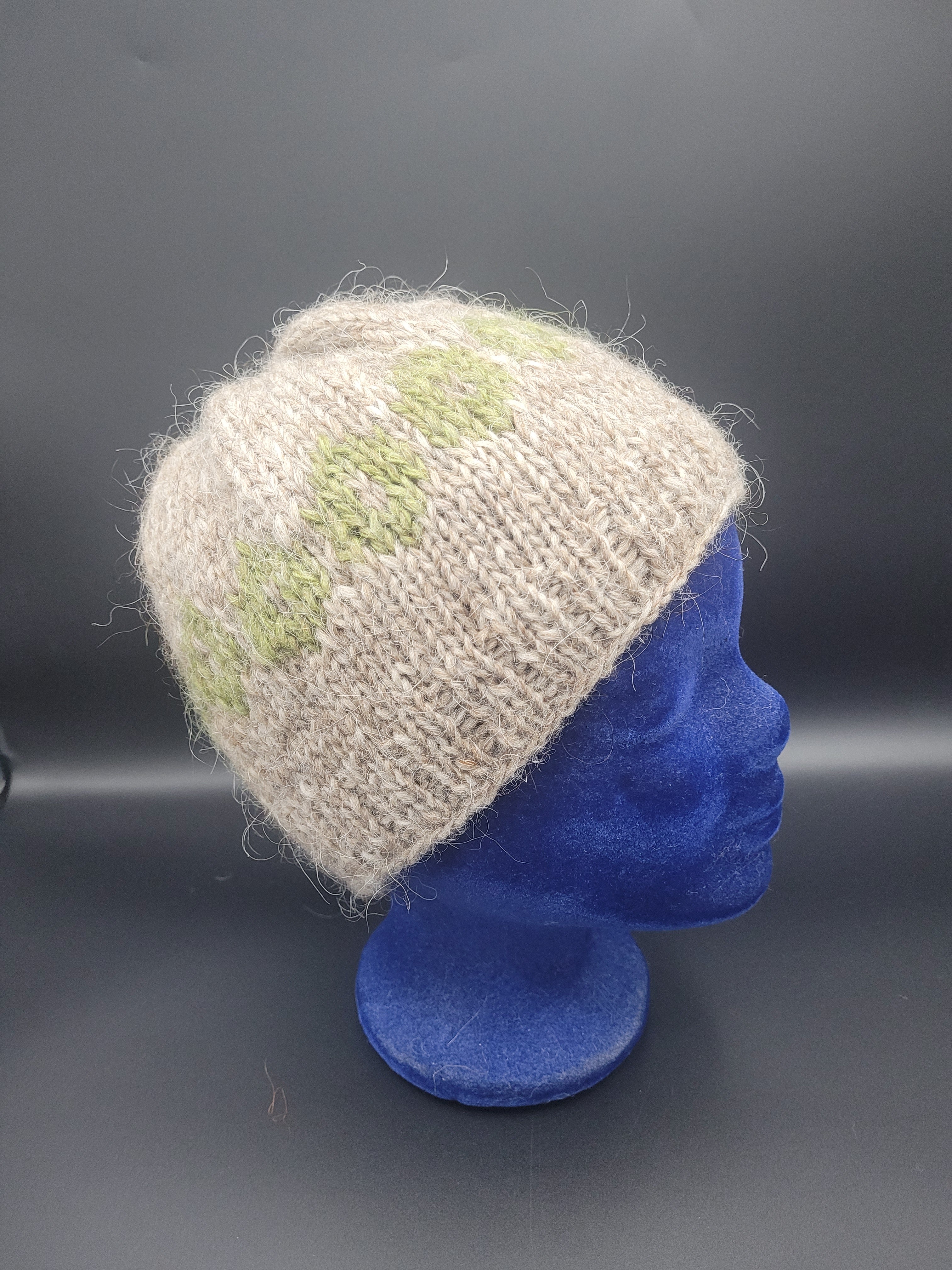 Beige knitted hat with a green pattern on a blue mannequin head.