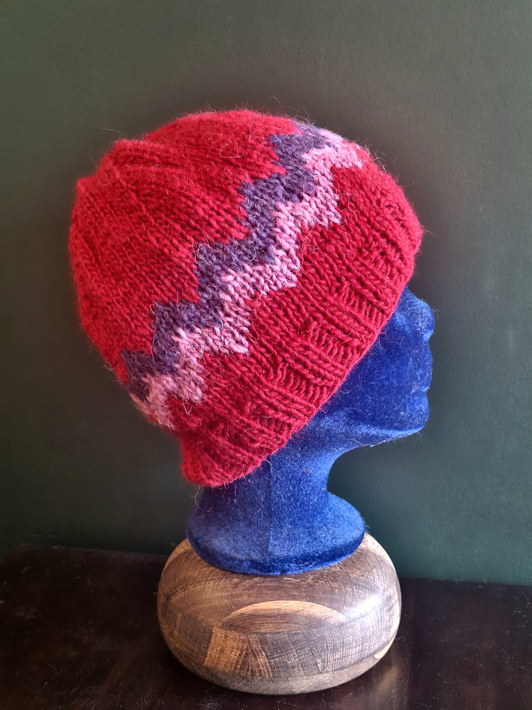 A knitted hat with a geometric pattern in red and blue, displayed on a mannequin head.