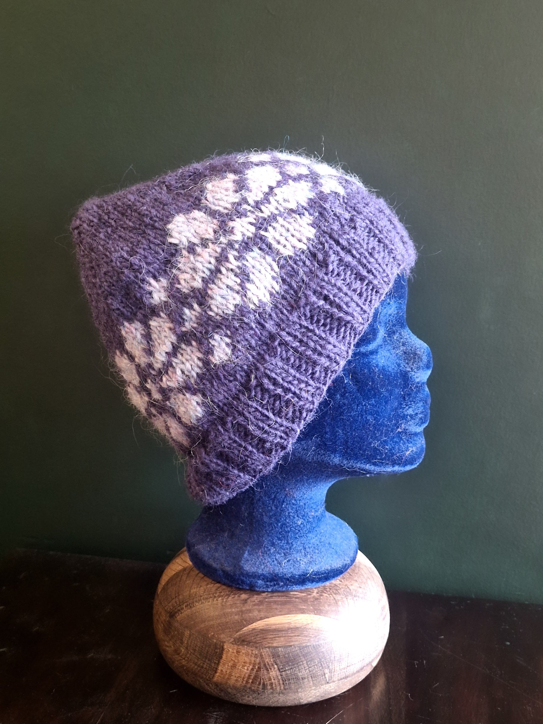 A knitted hat in purple with white flowers displayed on a mannequin head.