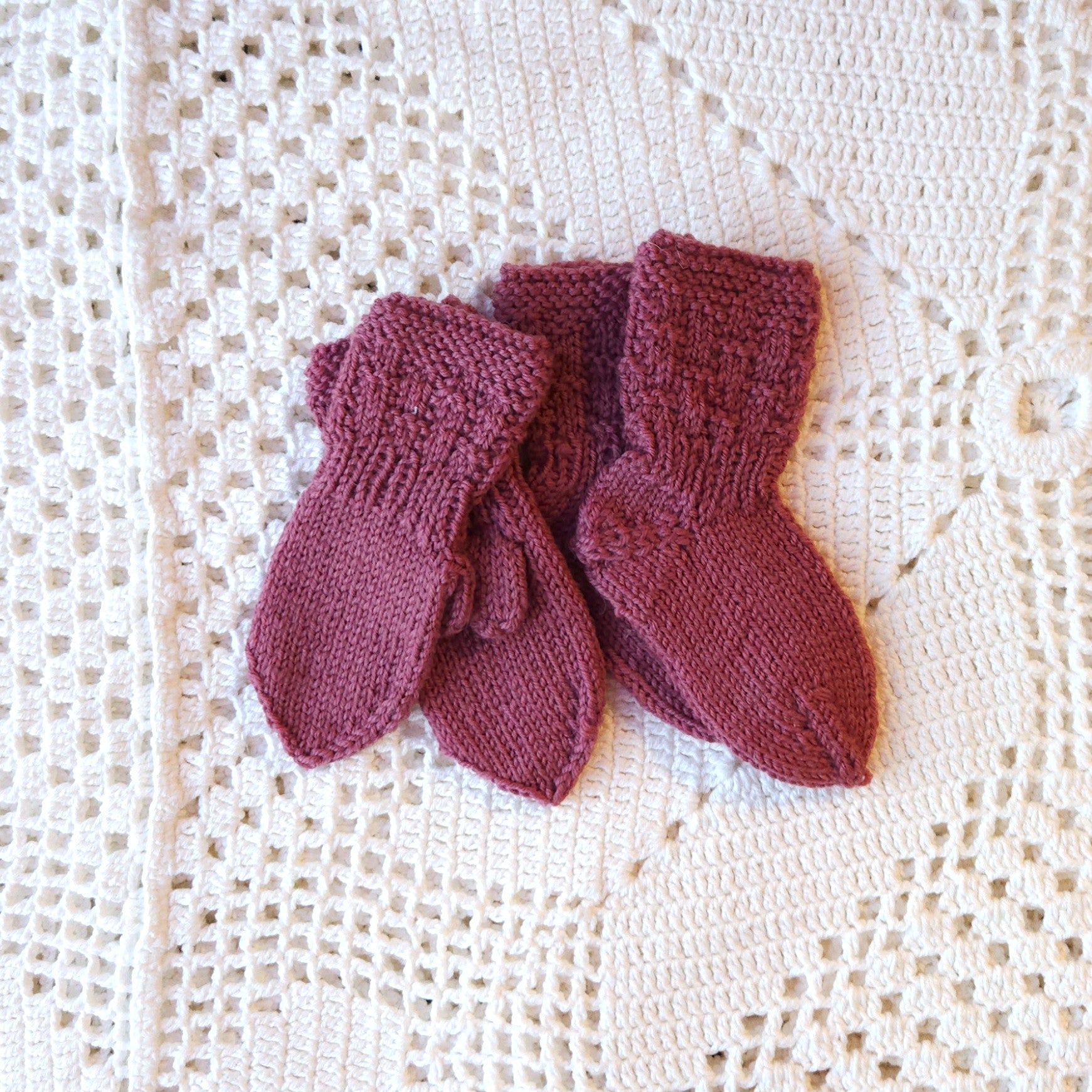 Pair of knitted baby socks and mittens on a textured white surface