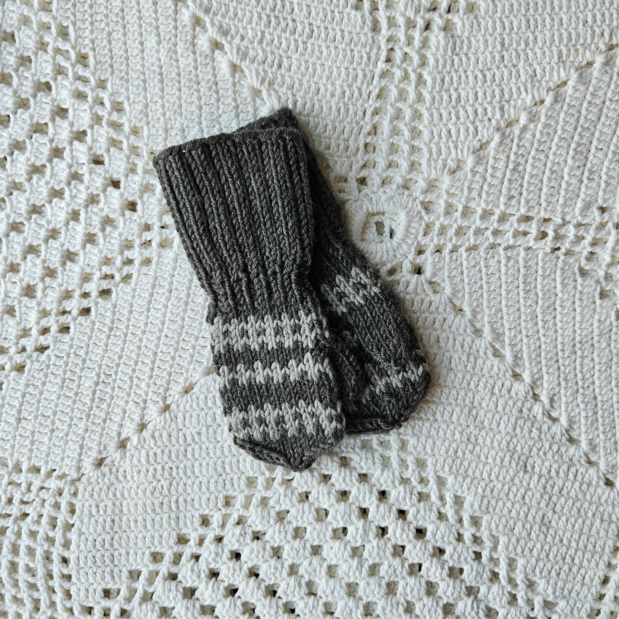 Pair of gray knitted mittens on a textured white fabric background