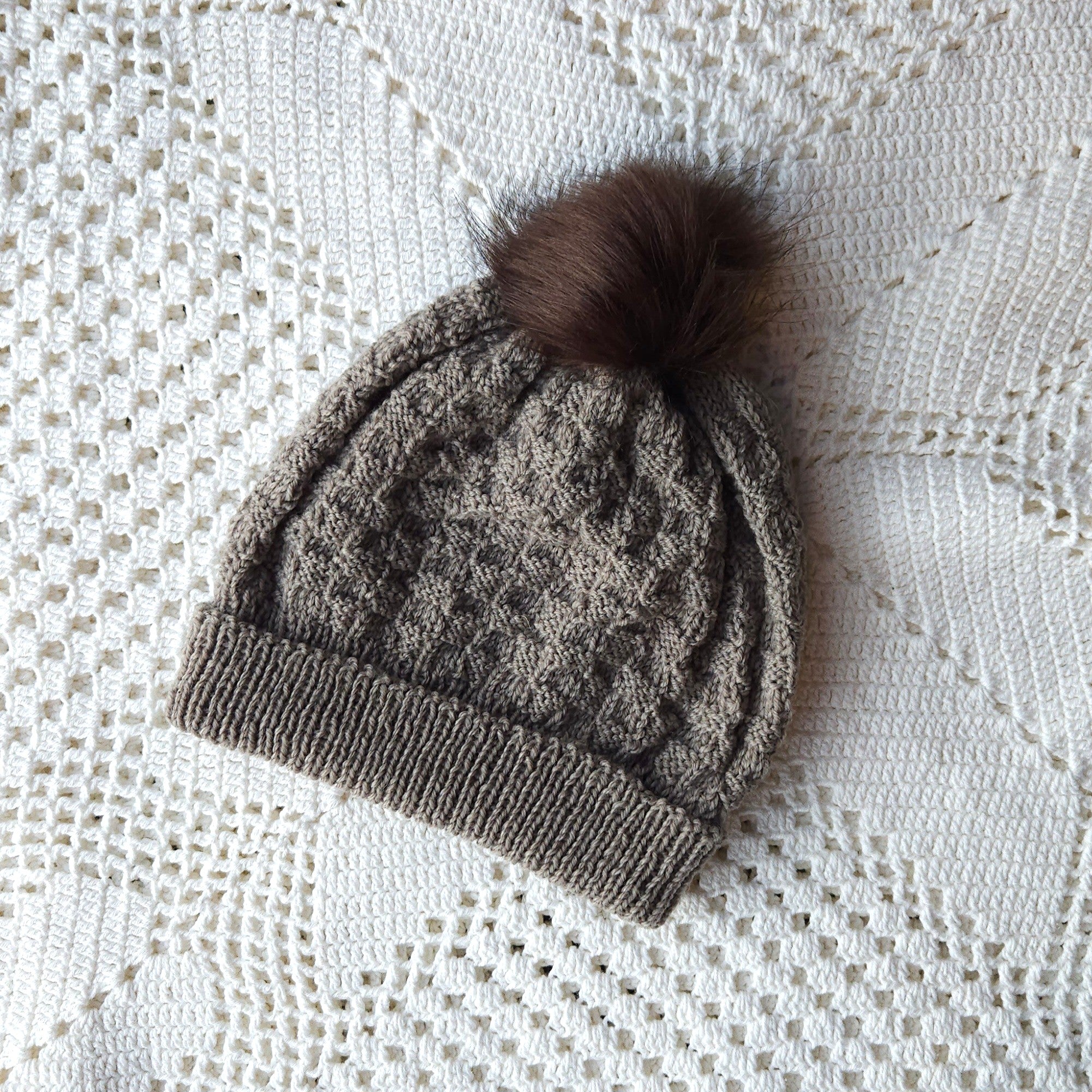 Knitted beanie with a brown pom-pom on a white textured surface
