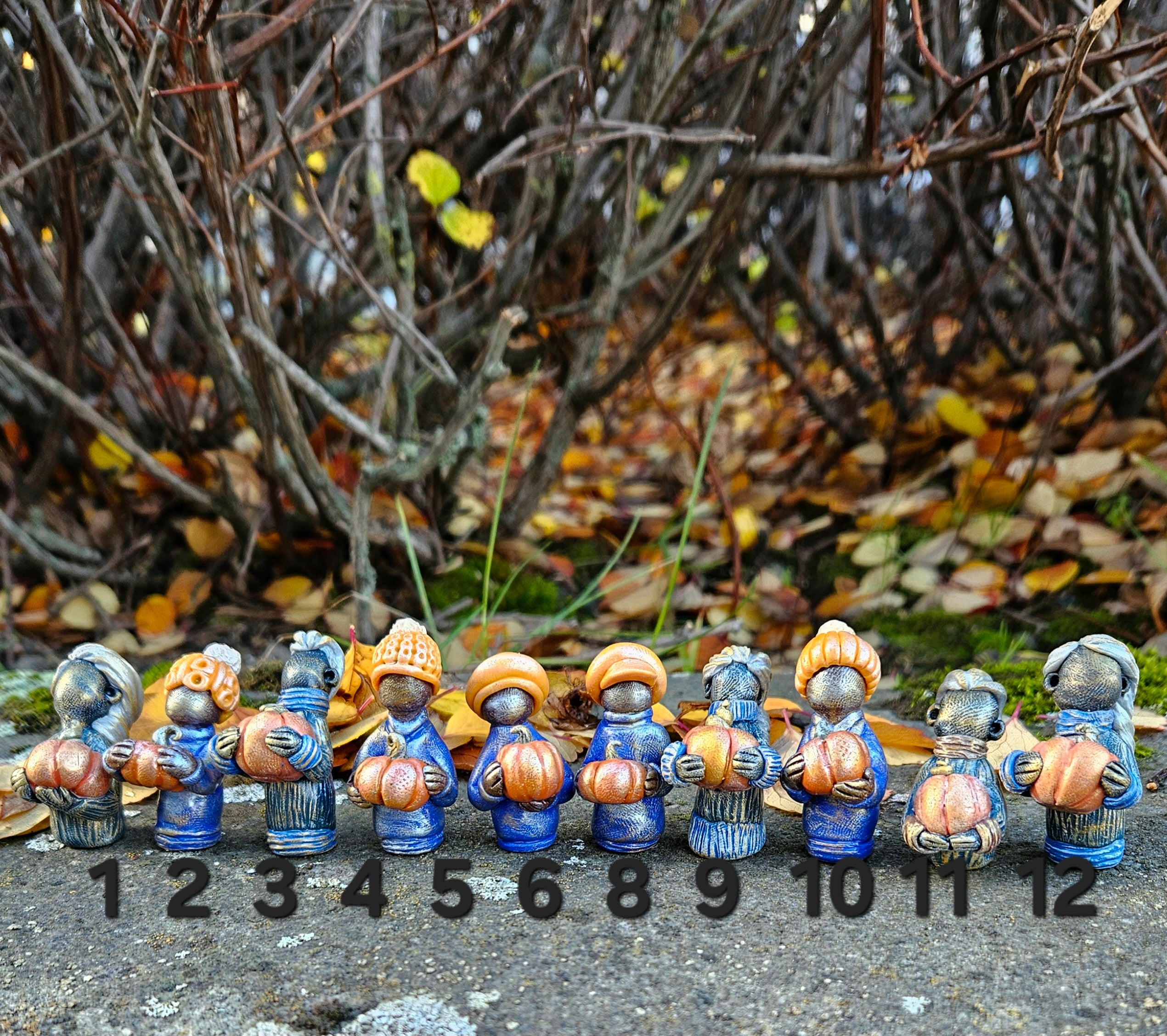 Row of small figurines with pumpkins against a natural background