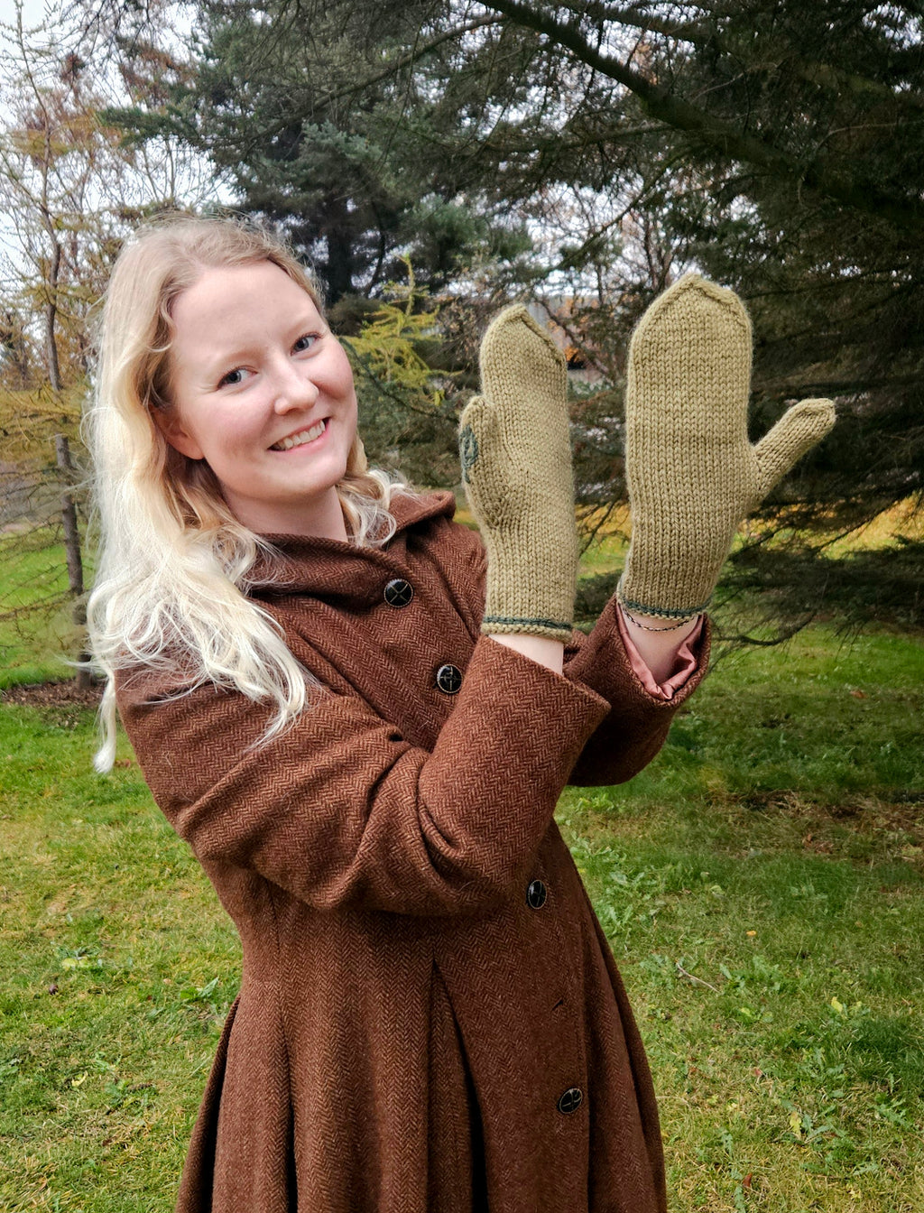 Person wearing a brown coat and green mittens outdoors with trees in the background