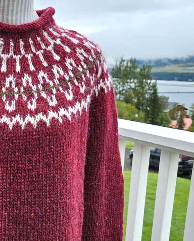 Red knitted sweater with white pattern on a railing with a scenic background