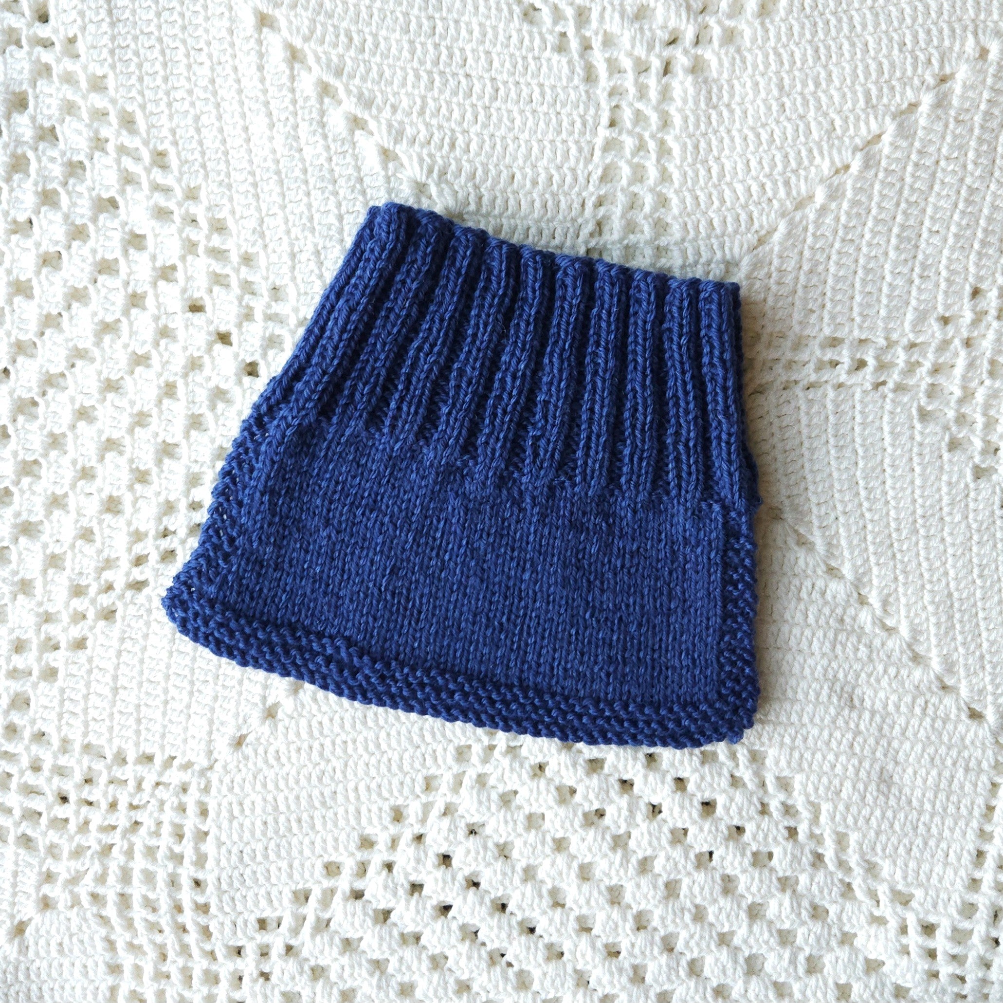 Blue knitted baby neck warmer on a white lace background