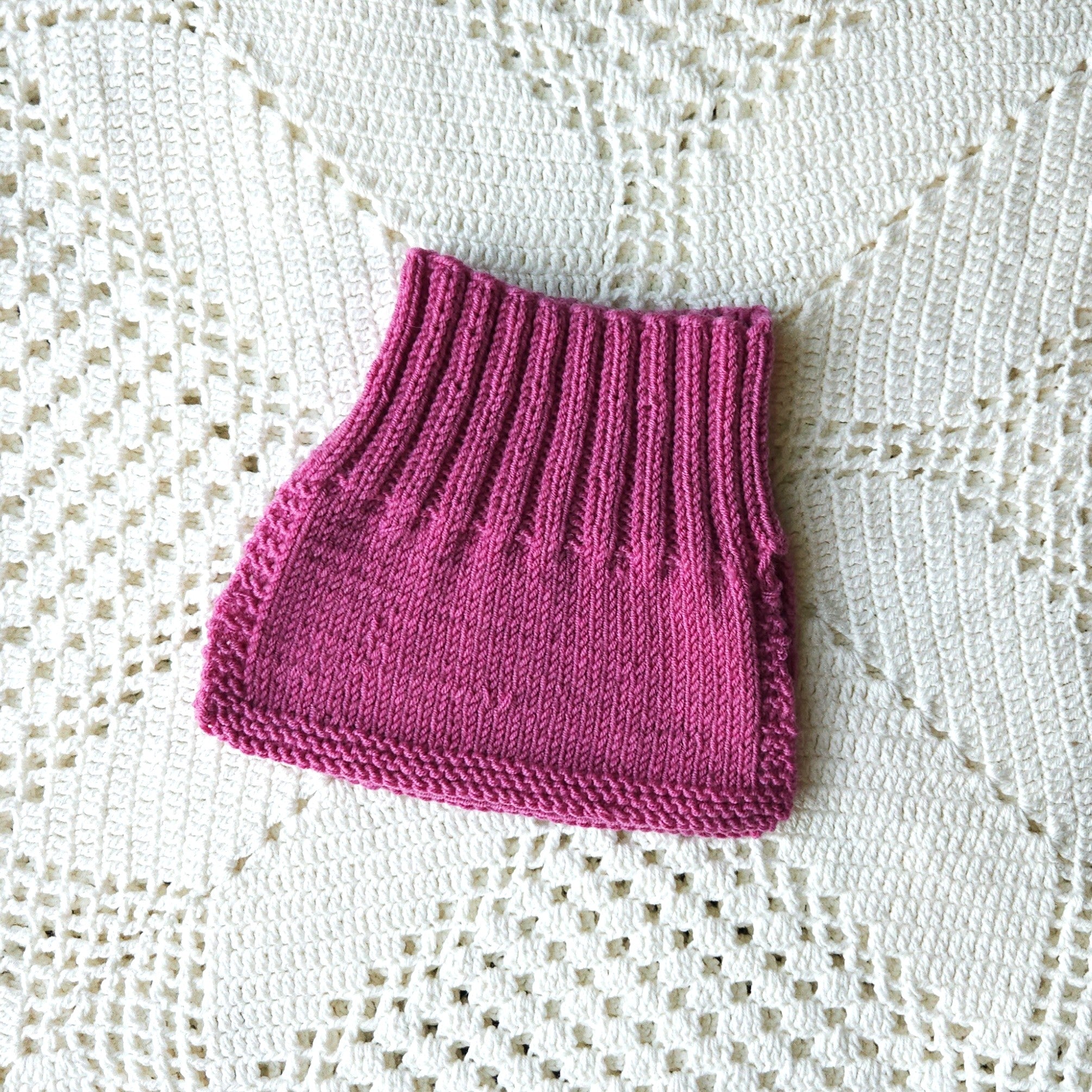 Pink knitted baby neck warmer on a white lace background