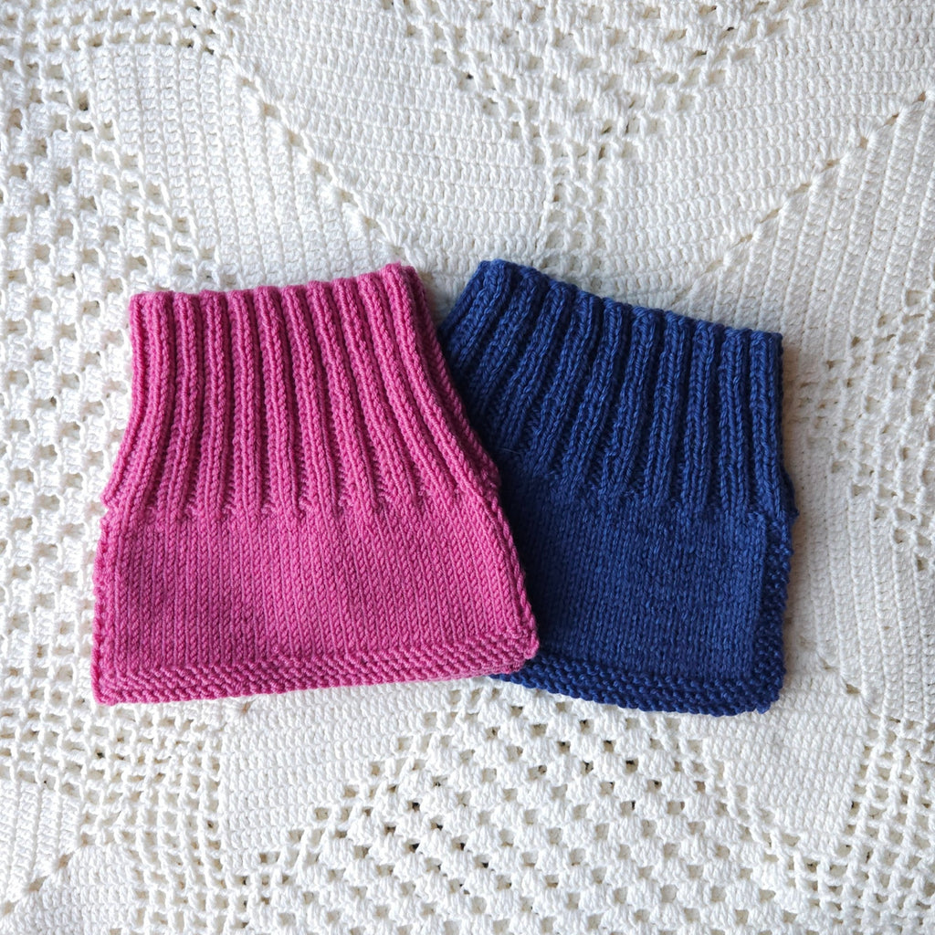 Pink and blue knitted baby neck warmers on a white lace background
