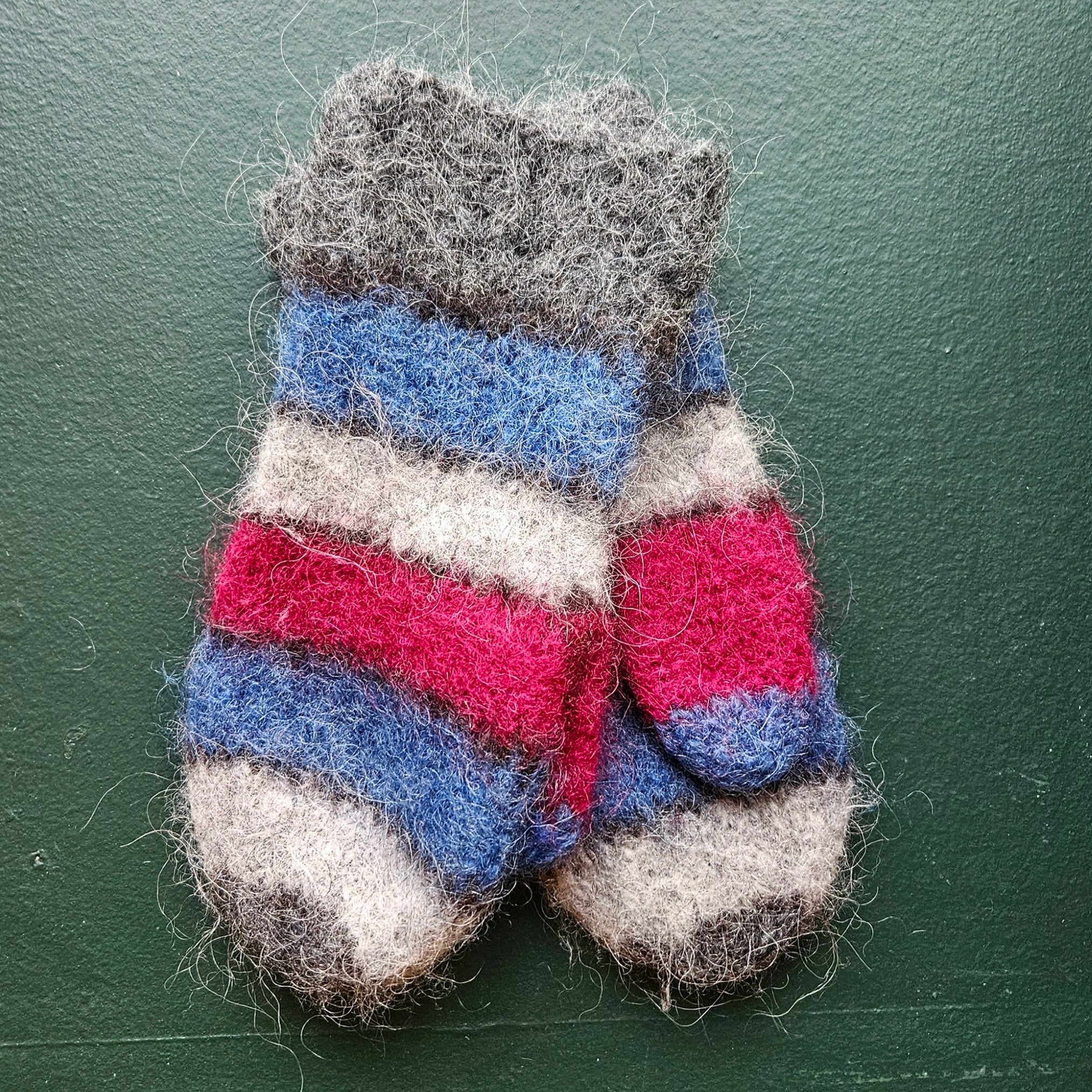 Pair of striped mittens in gray, blue, pink, and white on a green background