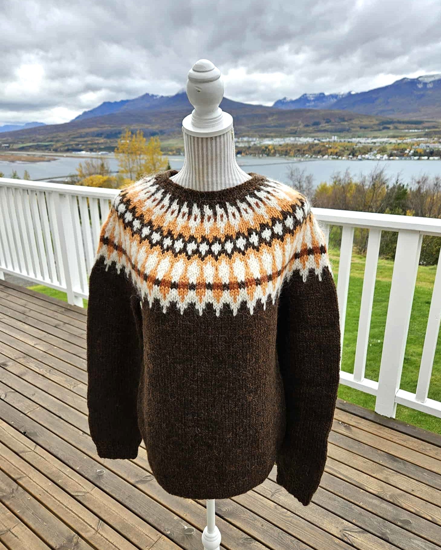Knitted sweater on a mannequin with a scenic background of mountains and water.