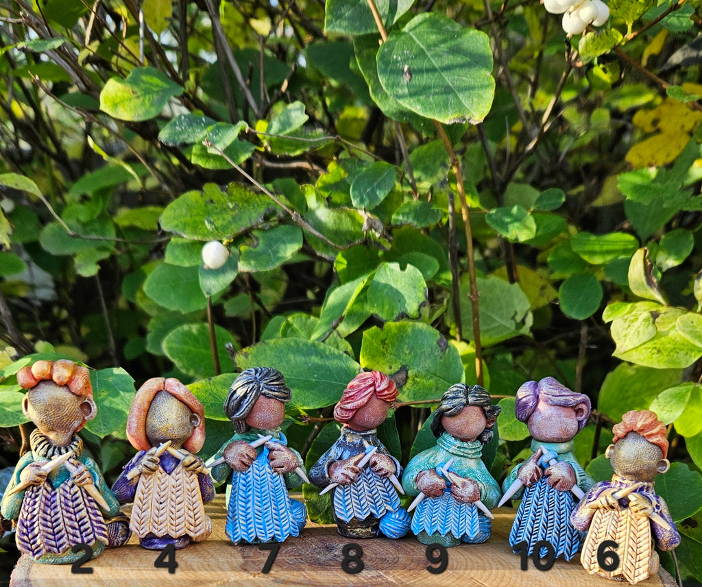 Set of small figurines with different hairstyles and clothing, standing on a wooden surface with green foliage in the background.