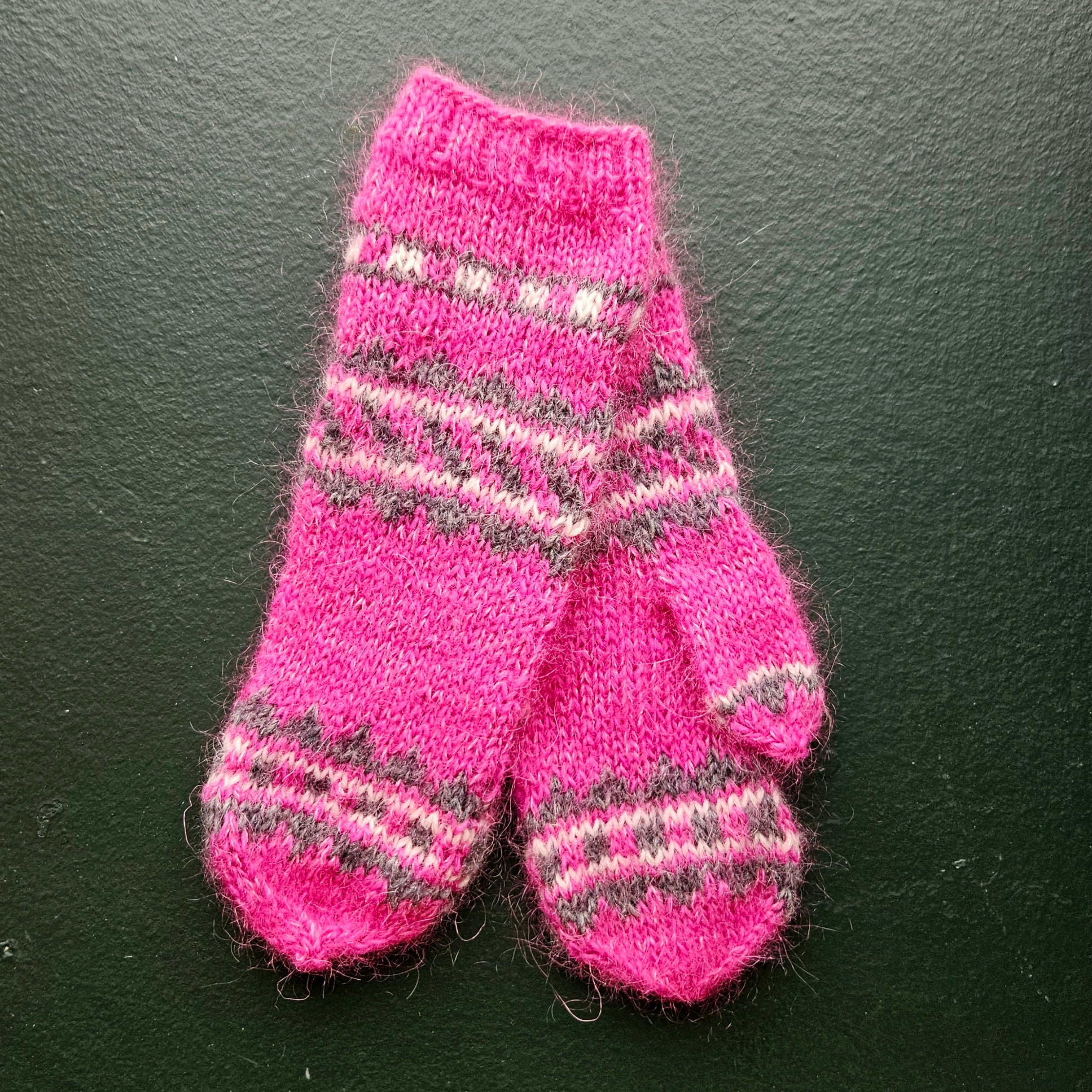 Pair of pink knitted kids mittenswith pattern on a dark background