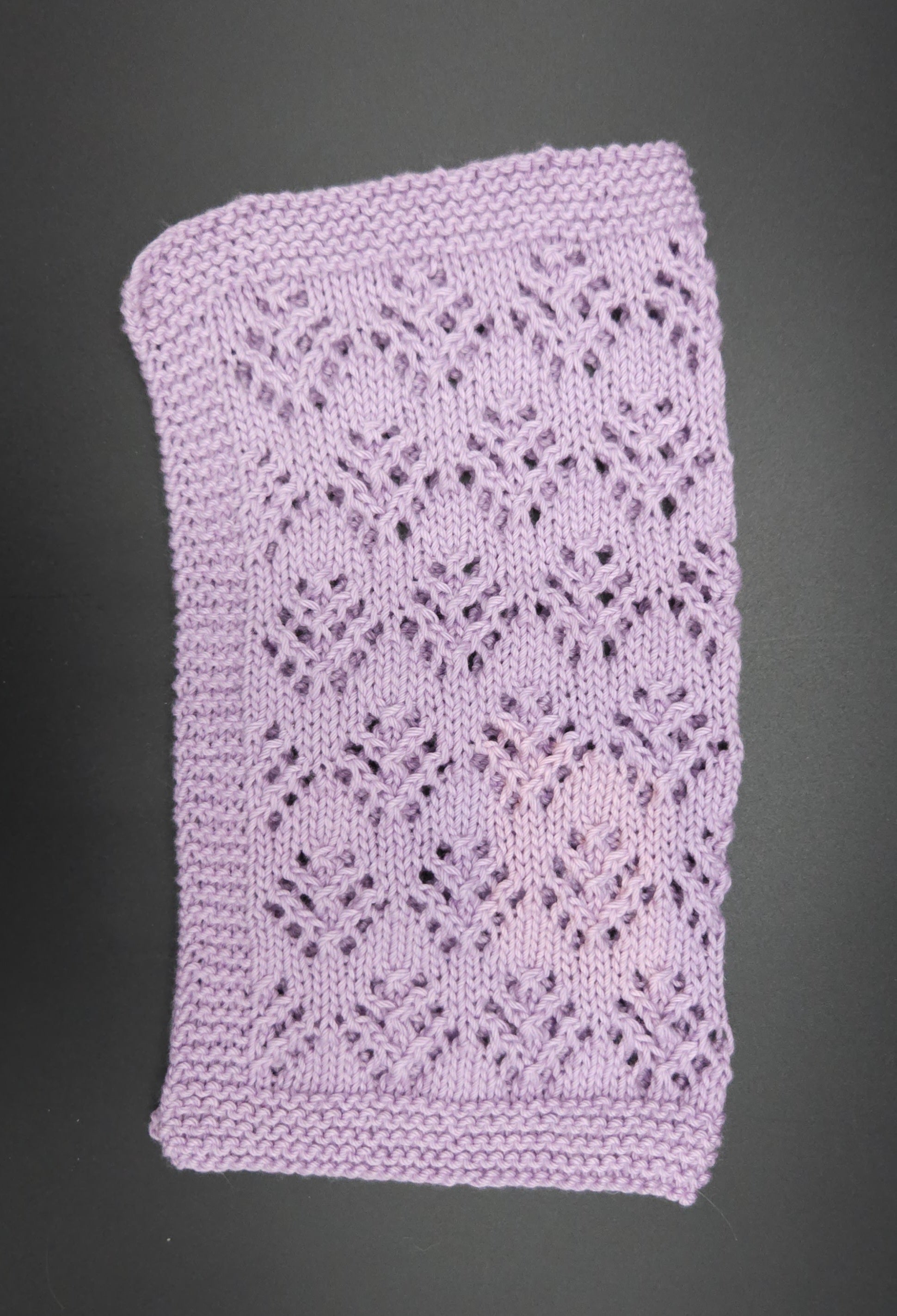 Purple knitted washcloth with a lace pattern on a black background