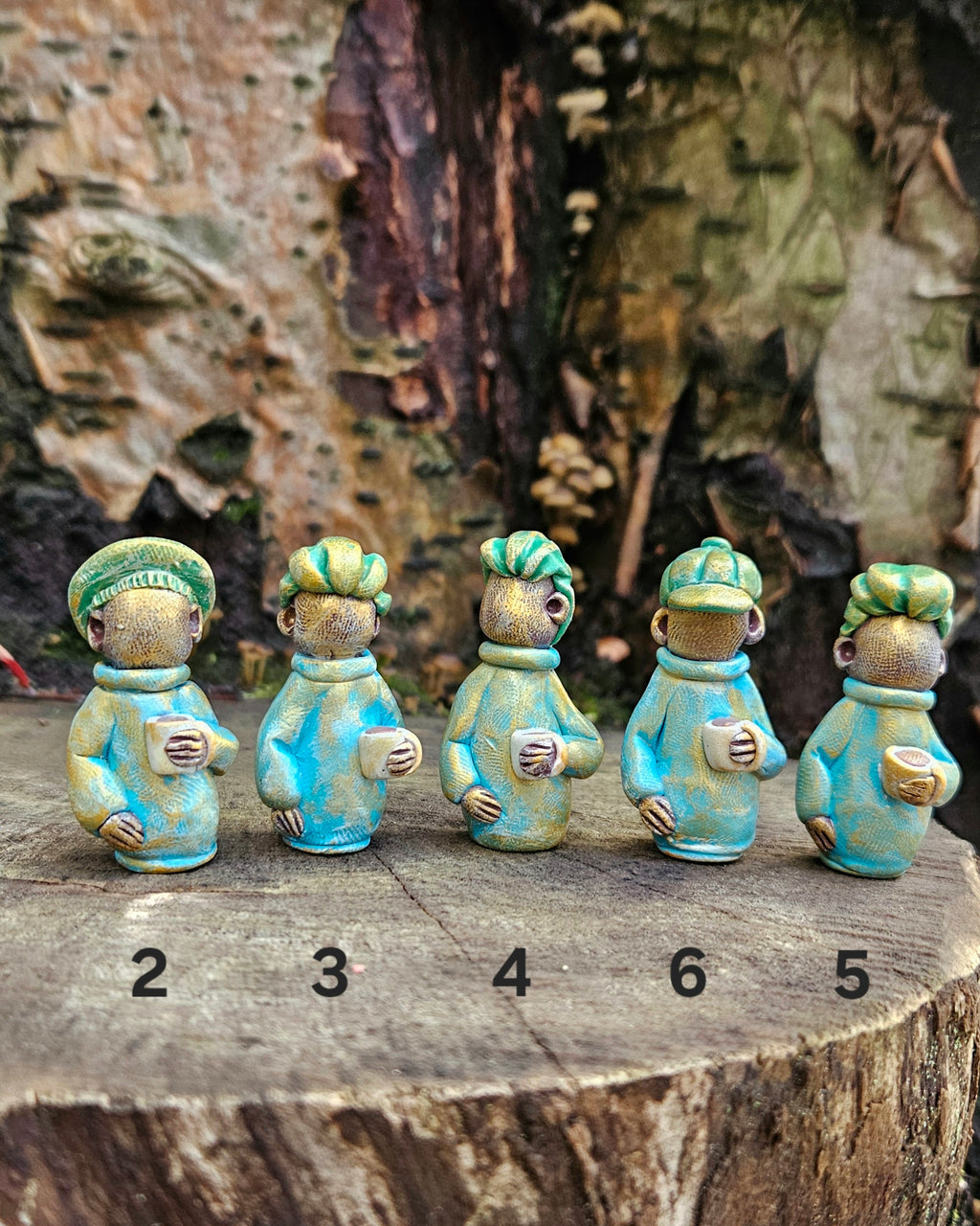 Five small ceramic figures with green hair and blue clothing on a wooden surface.