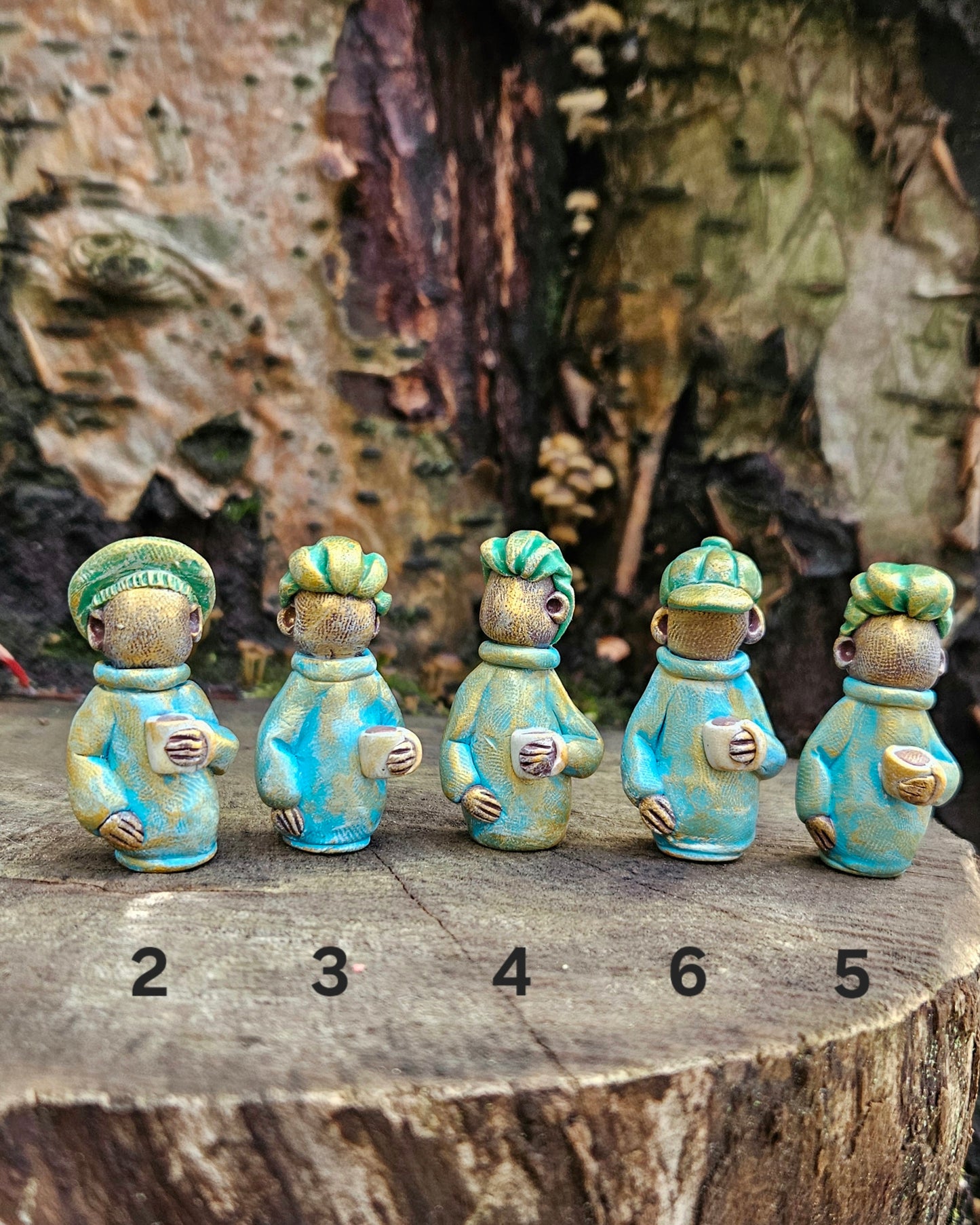 Five small ceramic figures with green hair and blue clothing on a wooden surface.