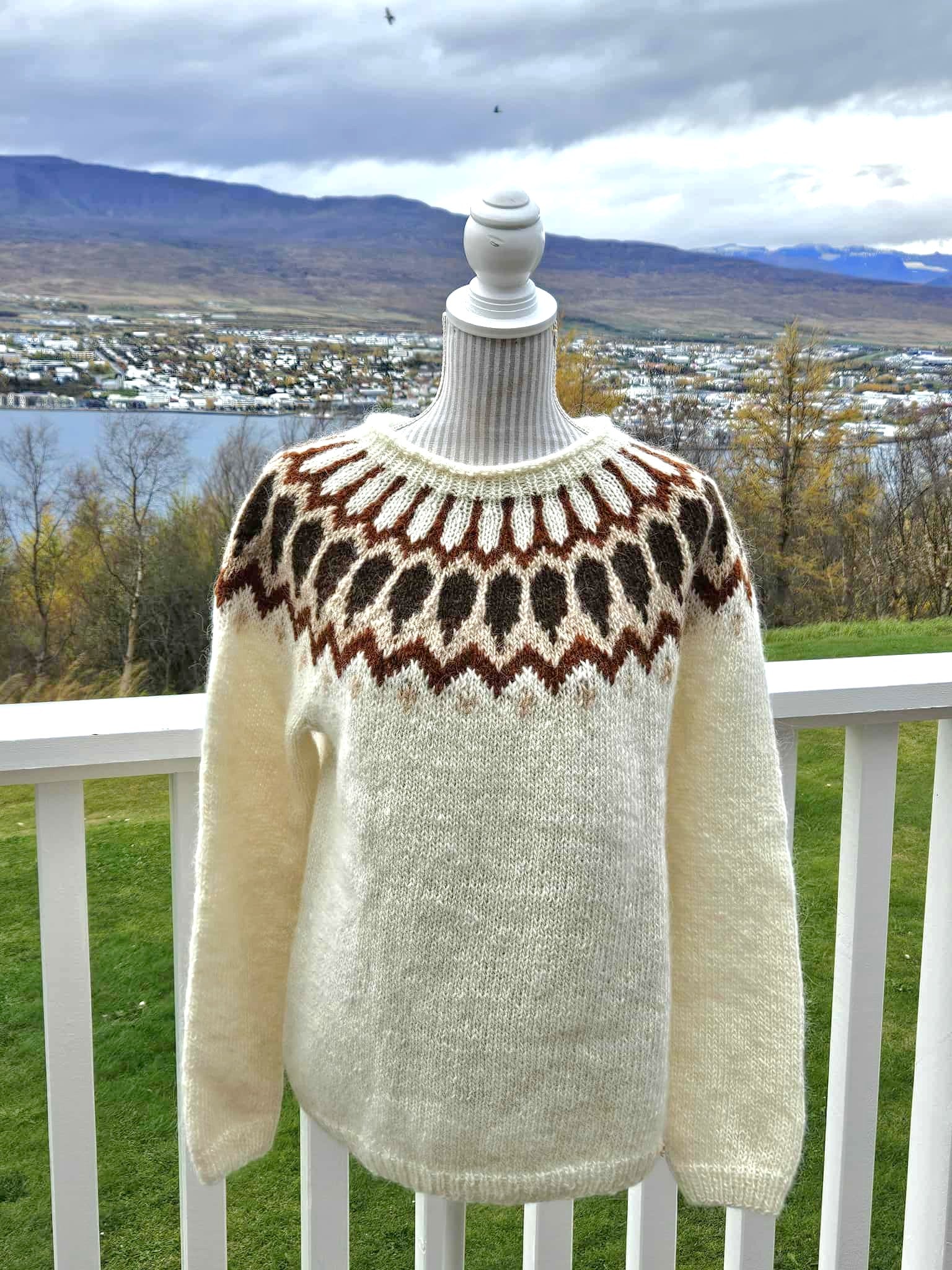 Knitted sweater with a pattern on a mannequin against a scenic background of mountains and water.