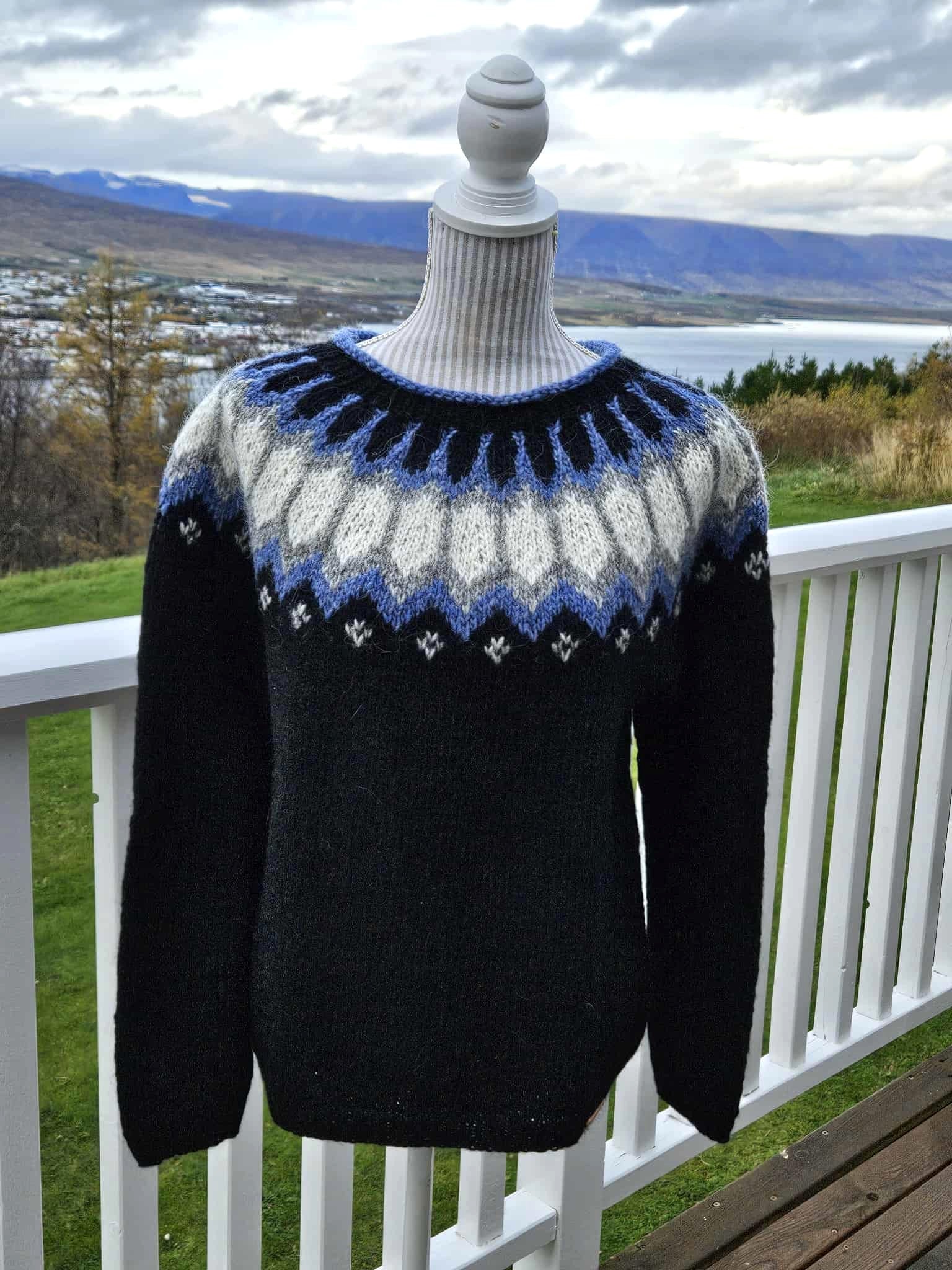 Black sweater with blue and white pattern on a mannequin against a scenic background