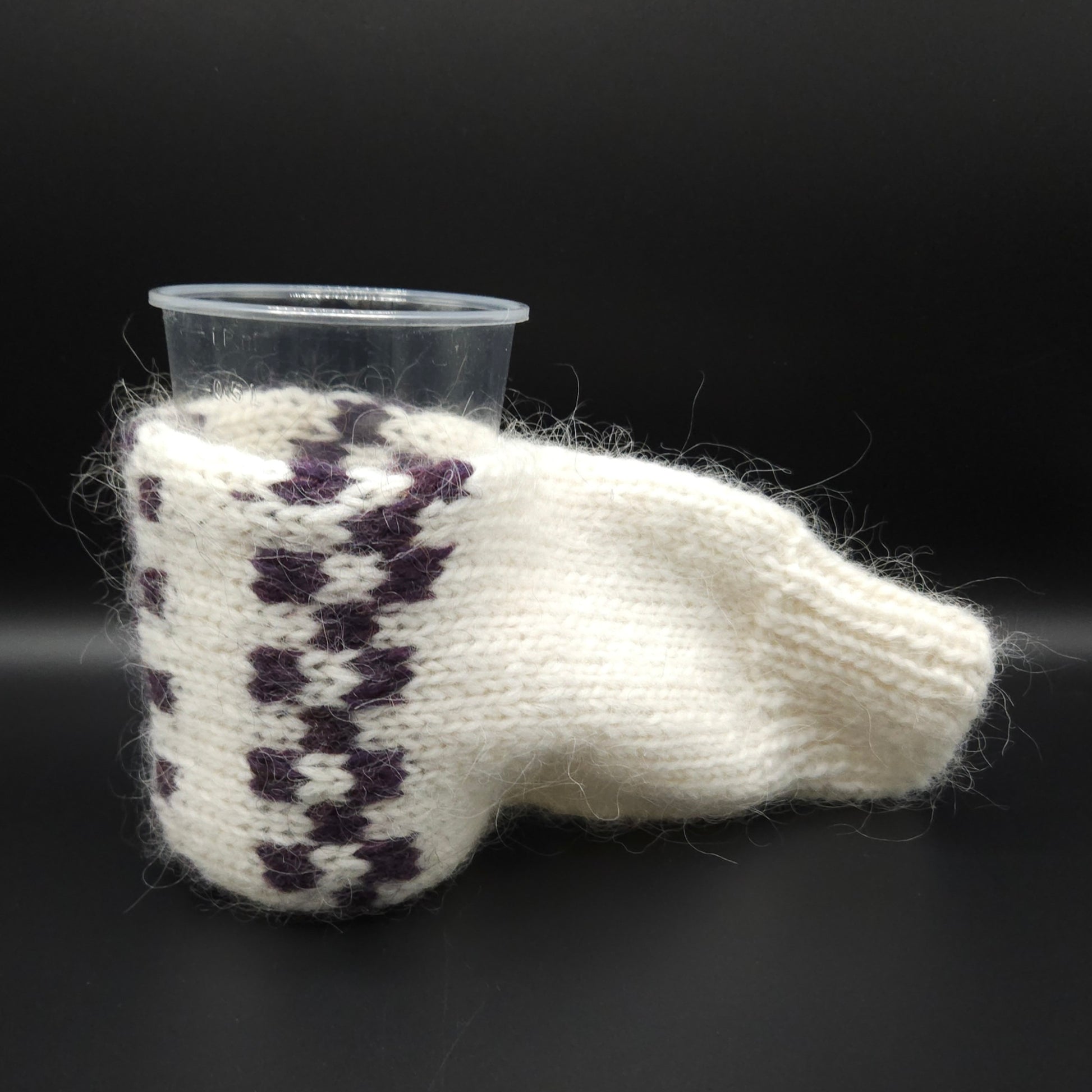 White knitted mitten for holding beer with purple pattern with a black background
